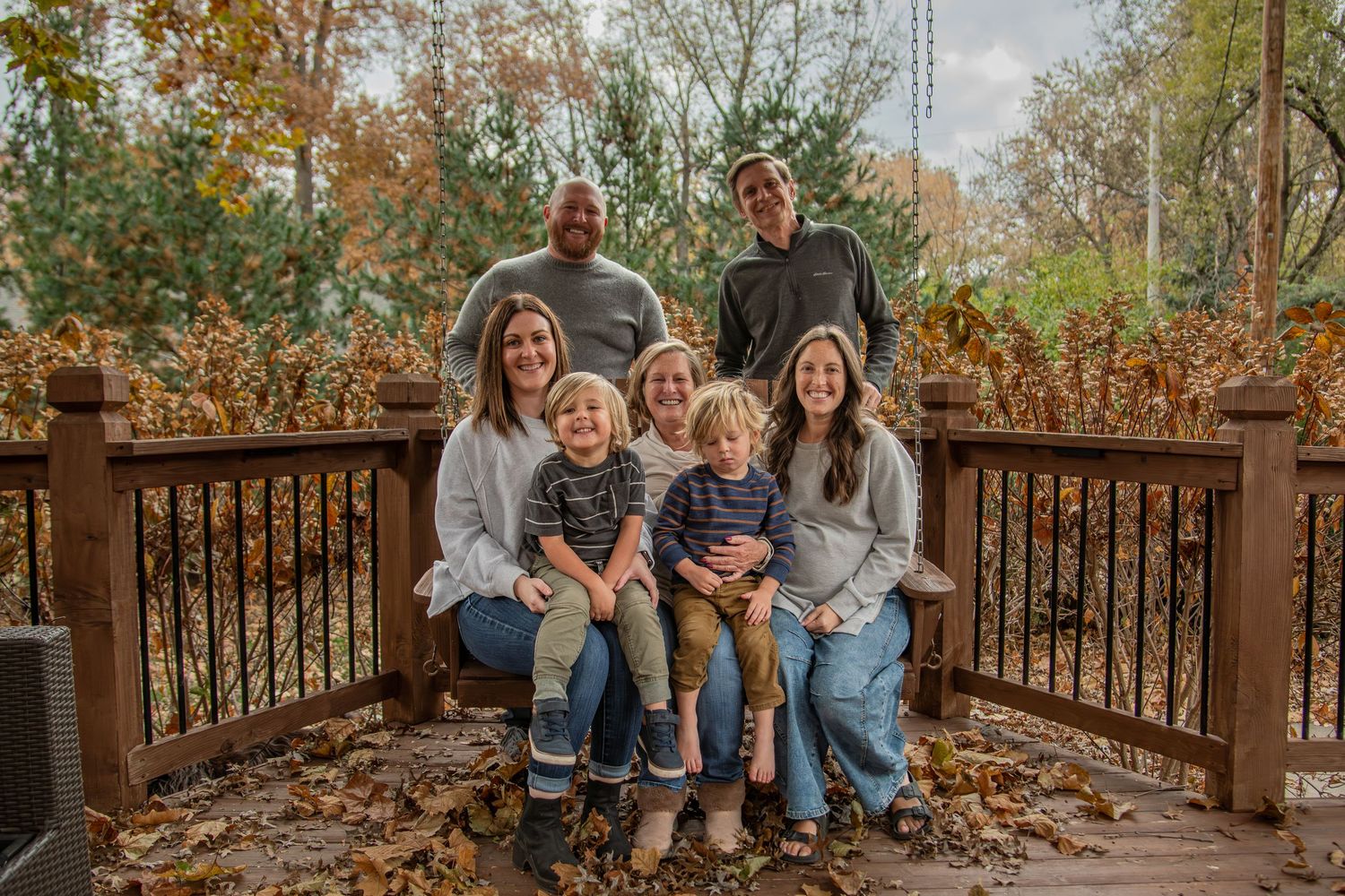 A casual group portrait on a wooden deck with autumn trees in the background.