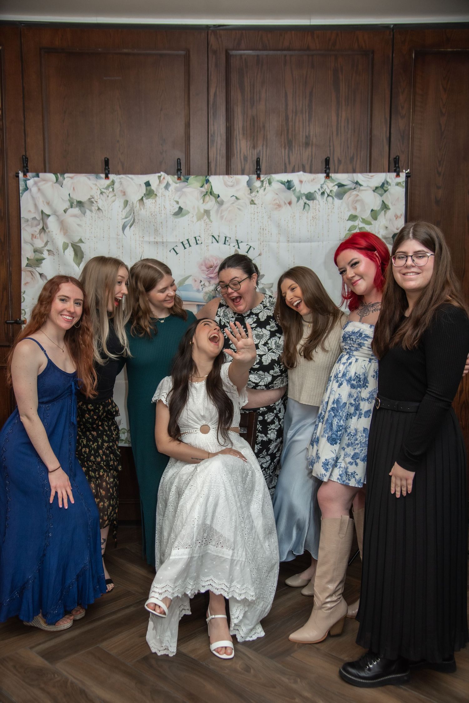 A group wearing formal attire poses for a fun photo in a row against a wall.