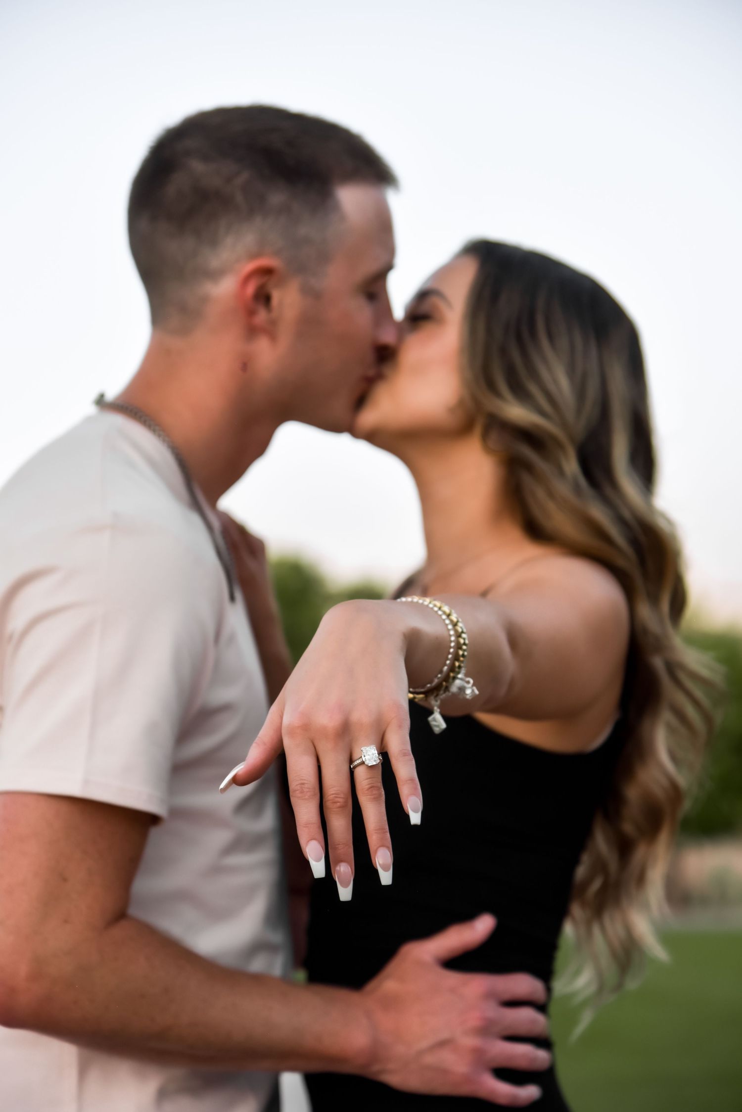 A romantic engagement photo series showing a couple embracing and kissing in an outdoor setting at sunset.