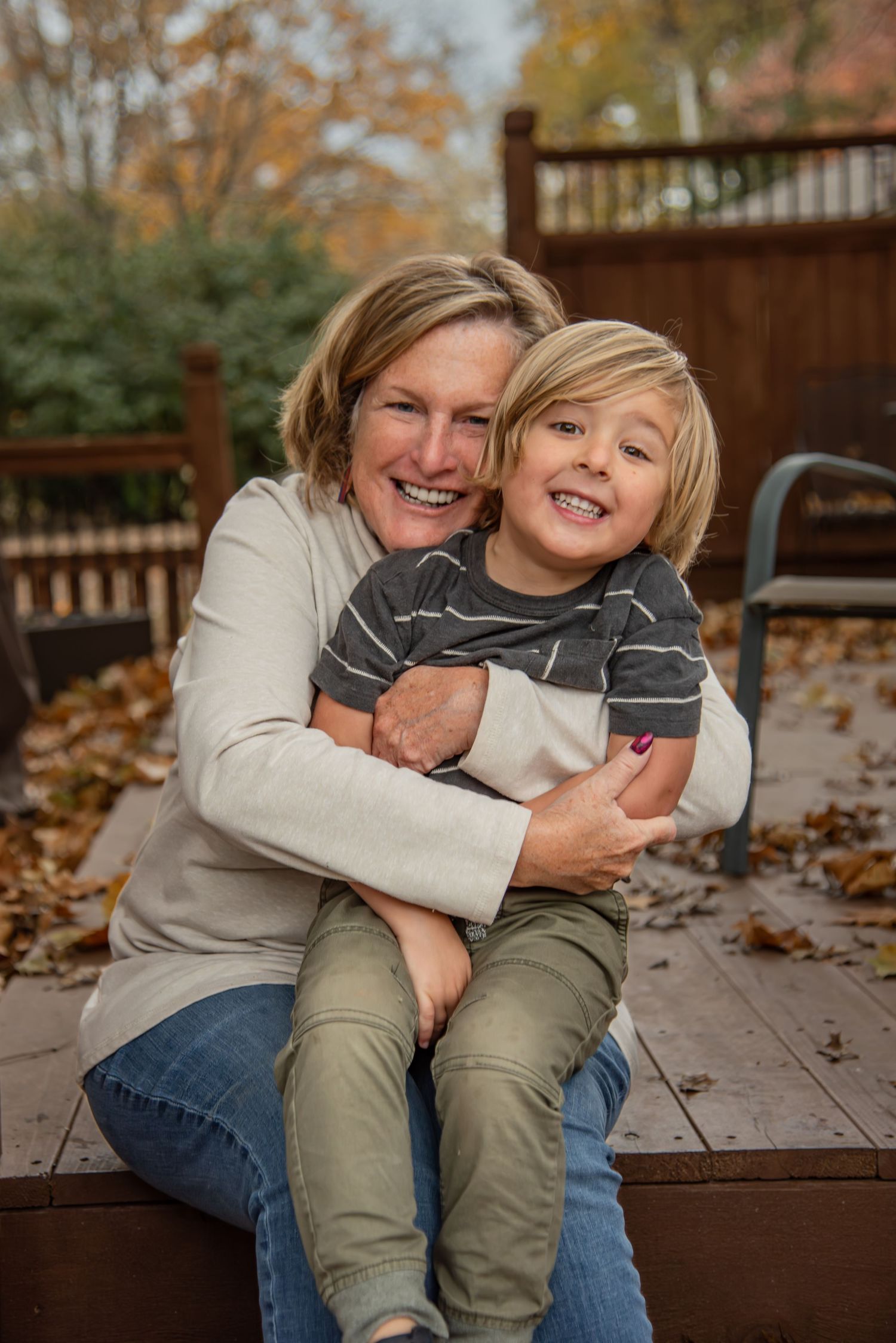 A playful moment captured on a wooden deck surrounded by autumn leaves as two people share warm embraces and laughter.