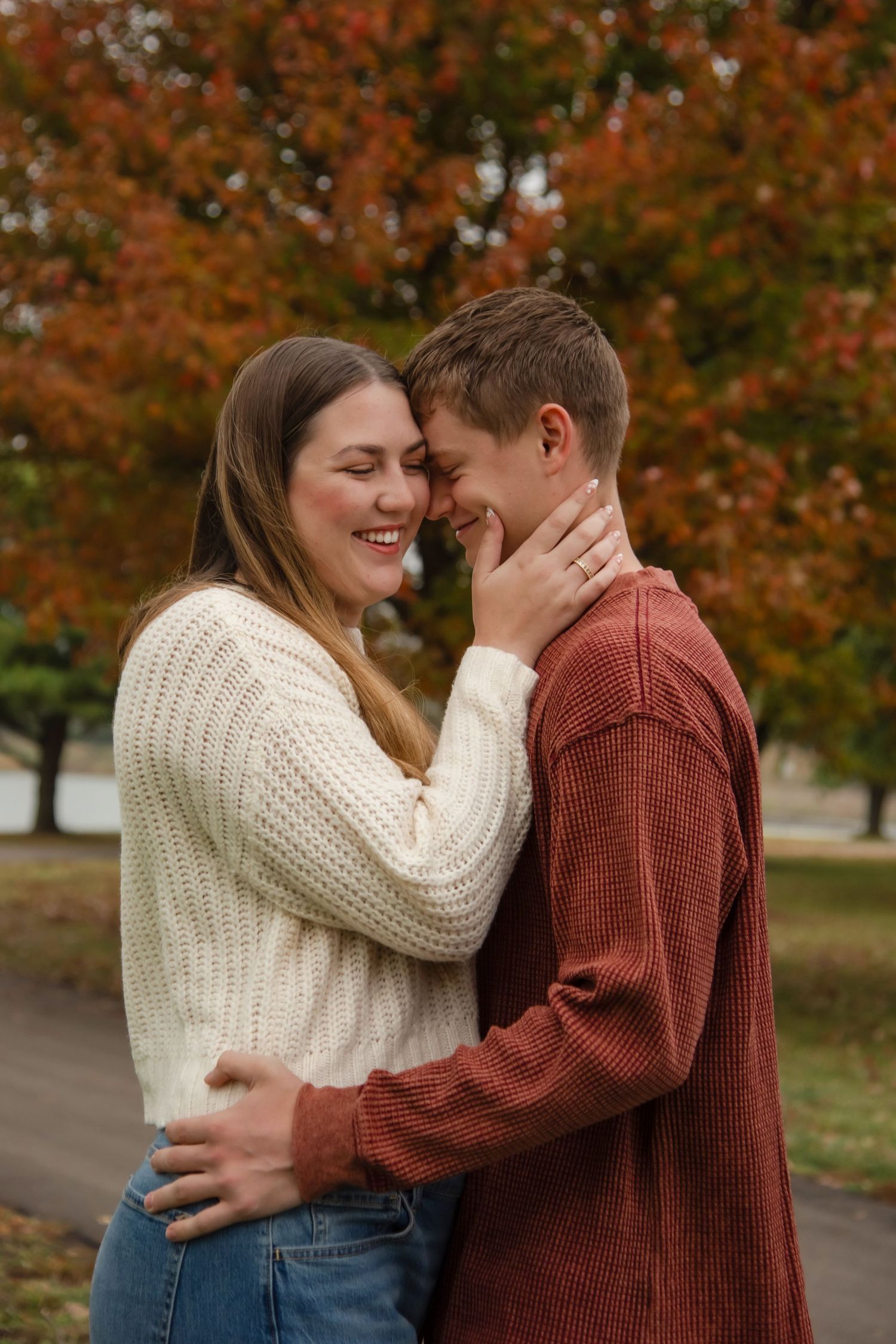 A couple shares an intimate moment while embracing outdoors against a backdrop of fall foliage.