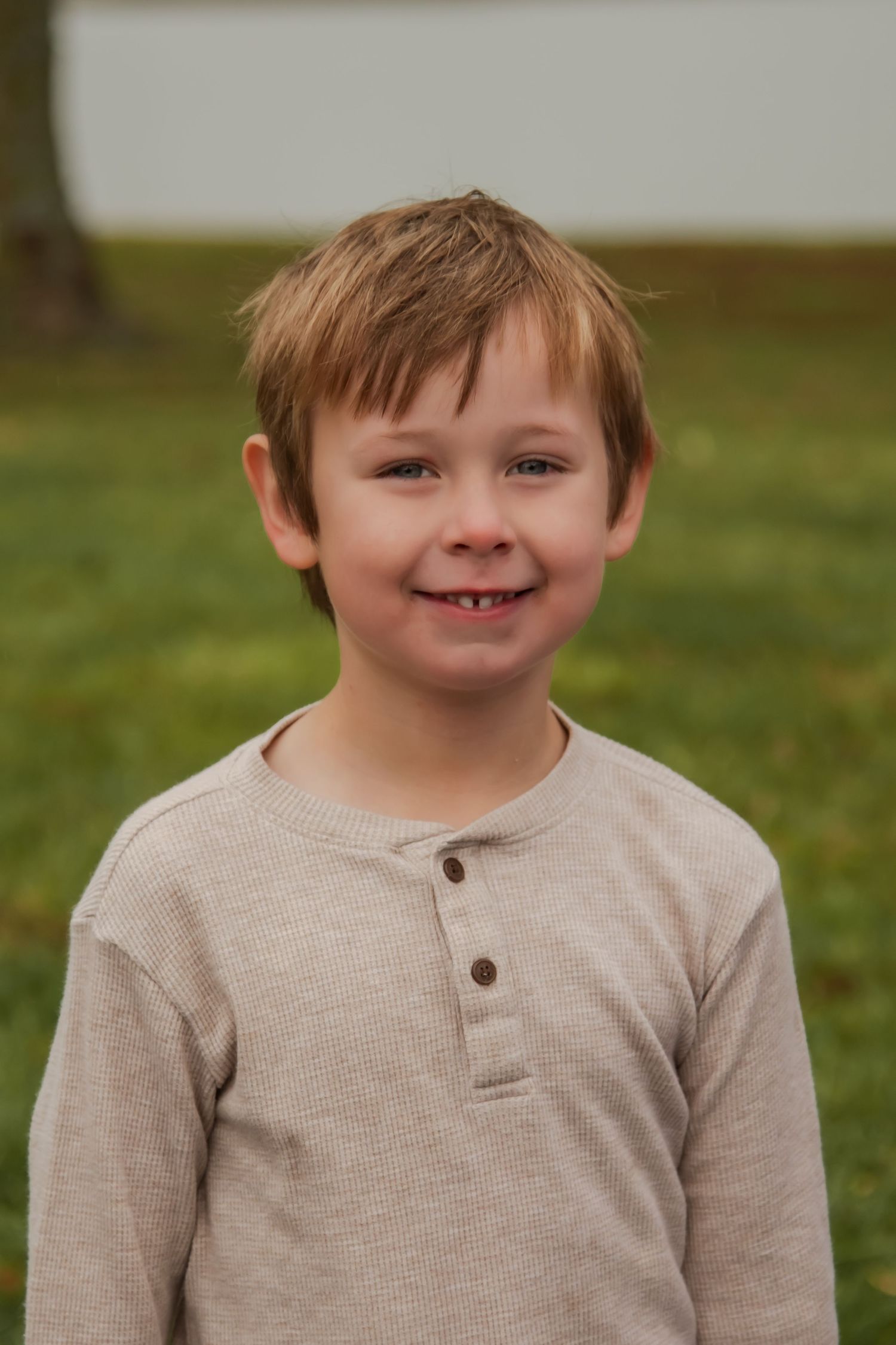 A child wearing a beige henley shirt smiles warmly at the camera.