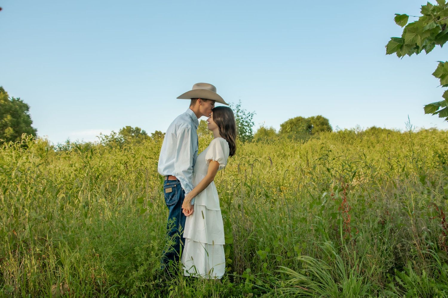 A couple walking hand in hand through a golden meadow at sunset in flowy summer outfits.