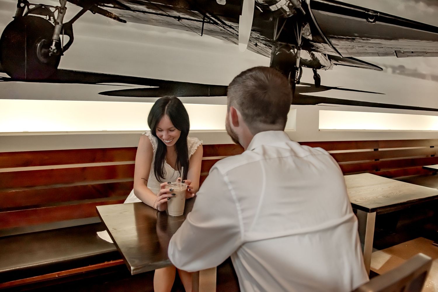 Two people sit at a table in conversation with boats visible in the background.