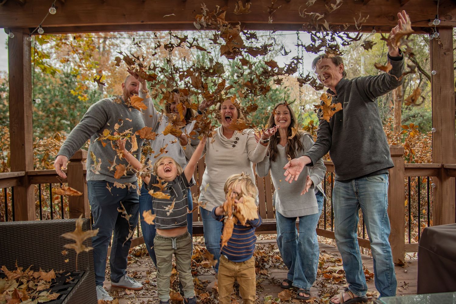 A group celebrates together on a wooden deck during fall season with leaves falling around them.
