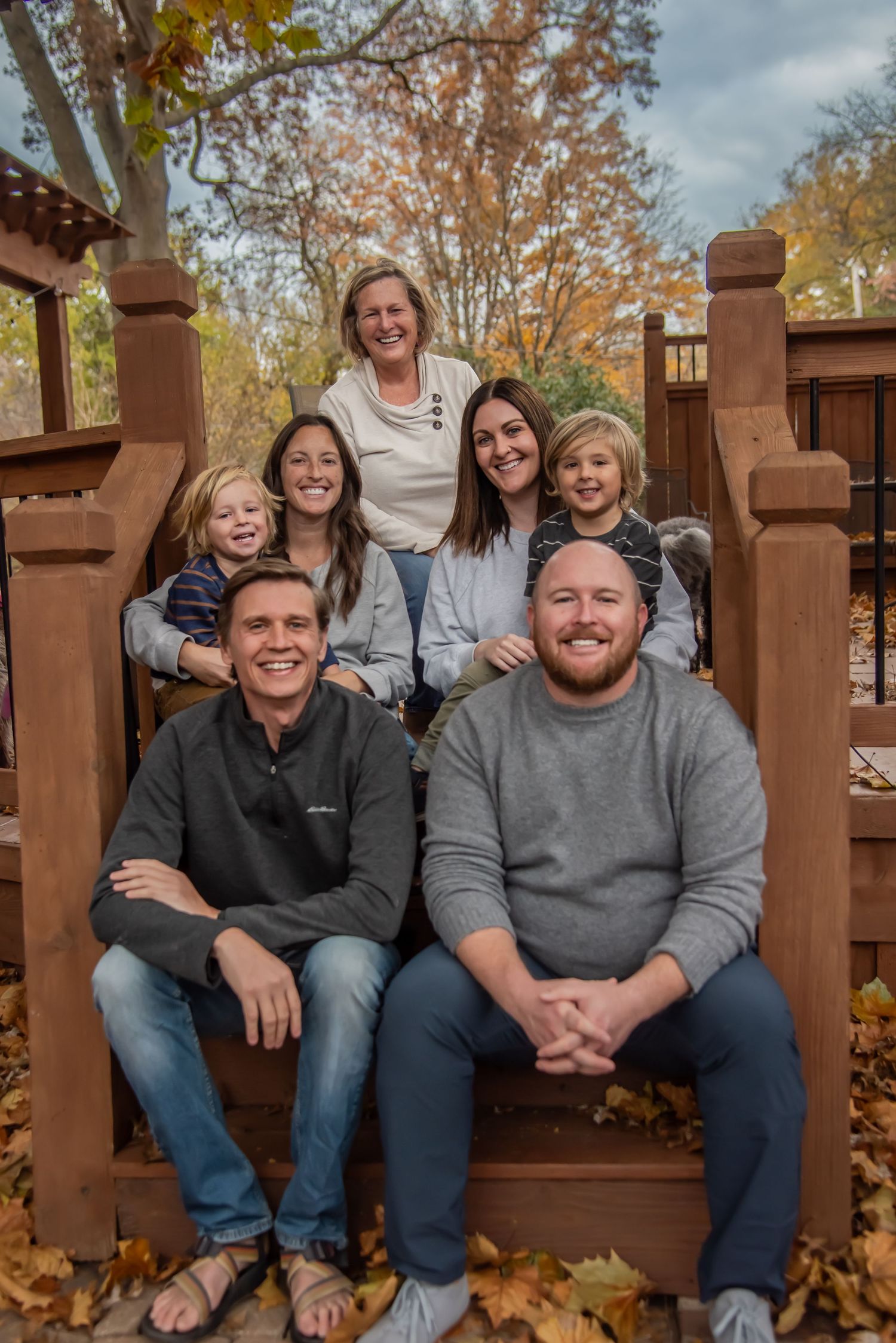 Family gathered on rustic wooden deck railing with autumn leaves scattered around during fall season.
