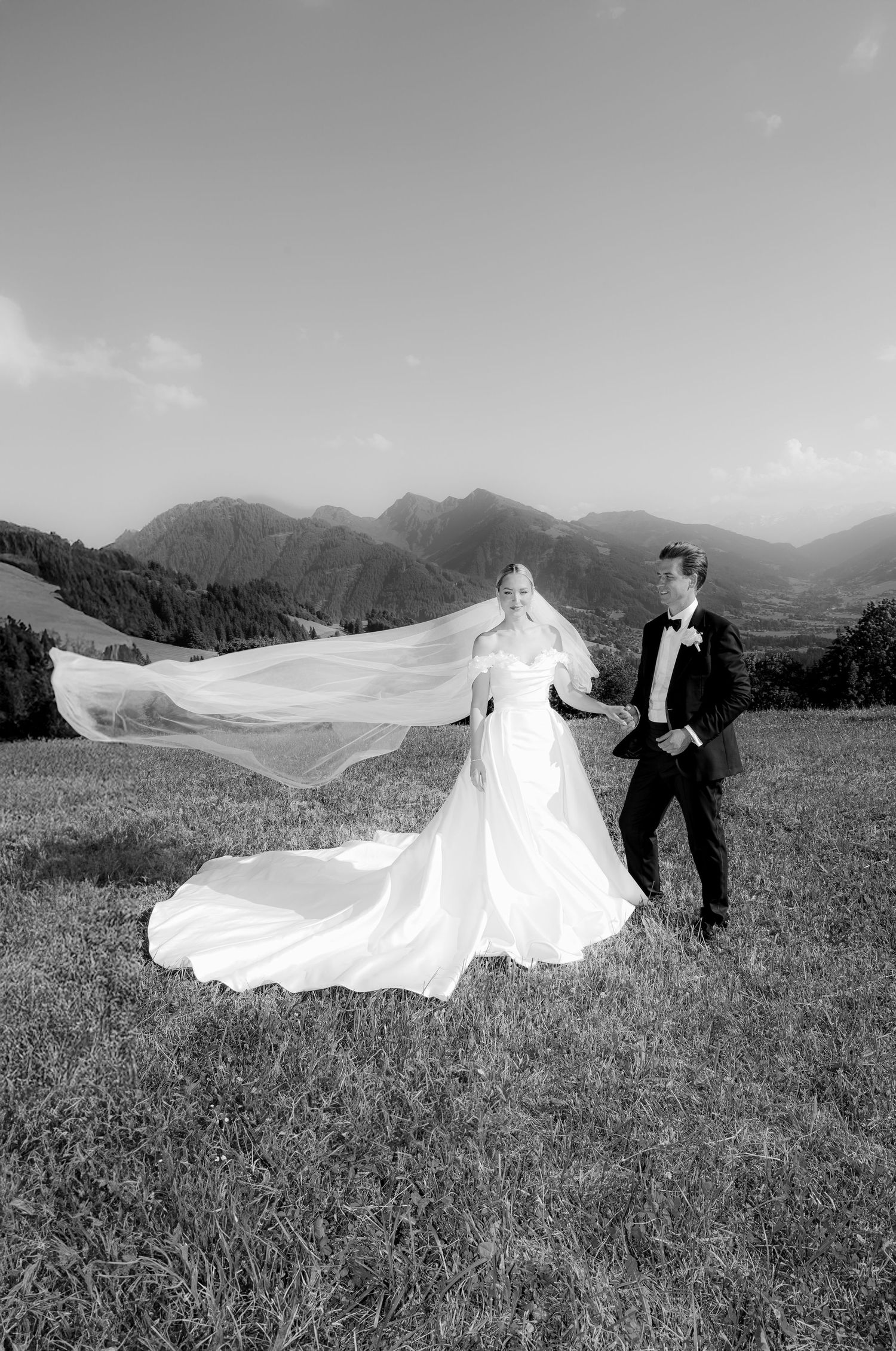 Wedding couple on mountain meadow with dramatic veil flowing in the wind.