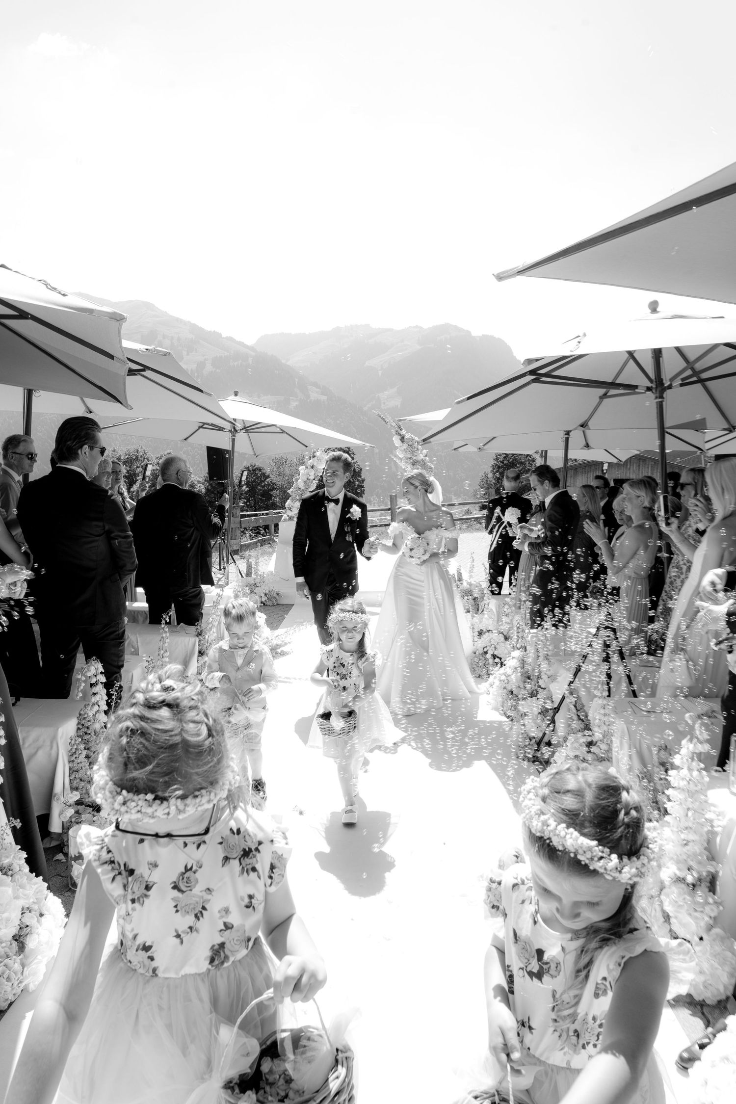Outdoor wedding reception under white umbrellas with mountain backdrop in black and white.