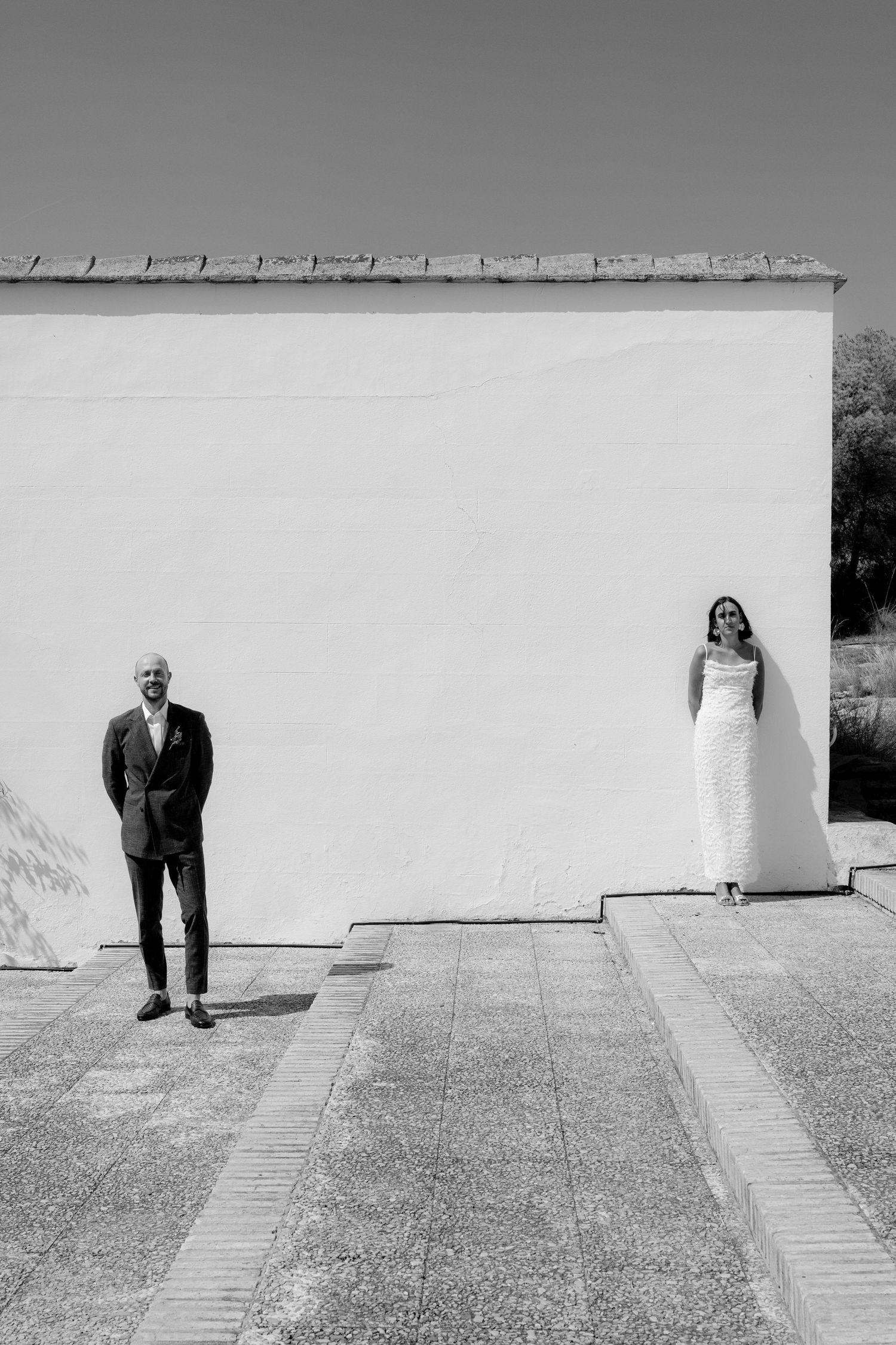 Artistic black and white sequence showing figures against stark white wall and paved path.
