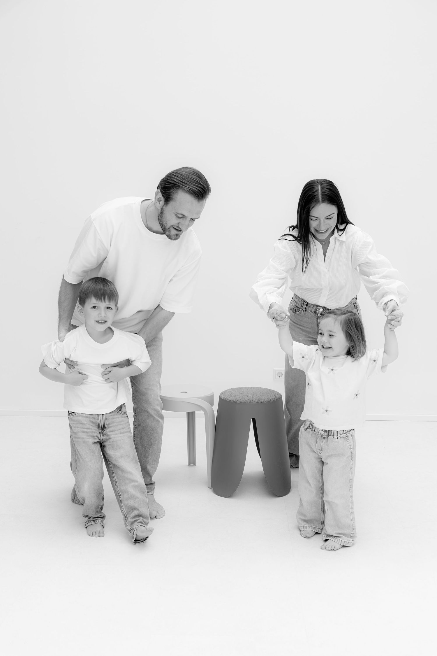 Black and white photo of a happy family with two young children playing together in a bright studio setting.