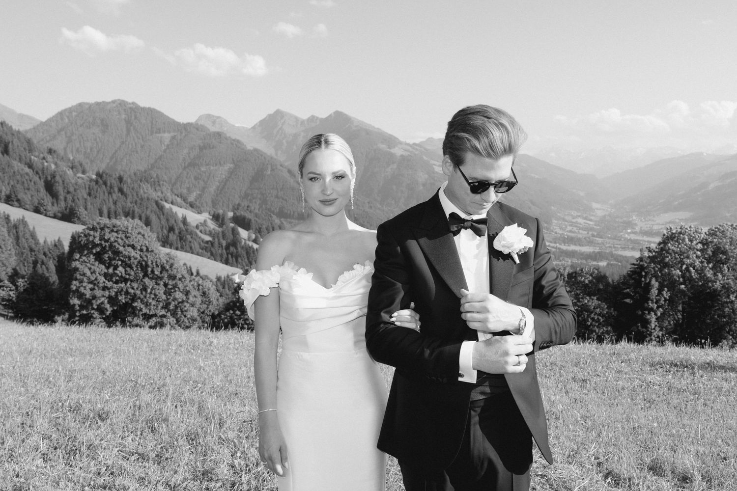 Wedding couple posing in mountain meadow with scenic alpine backdrop.