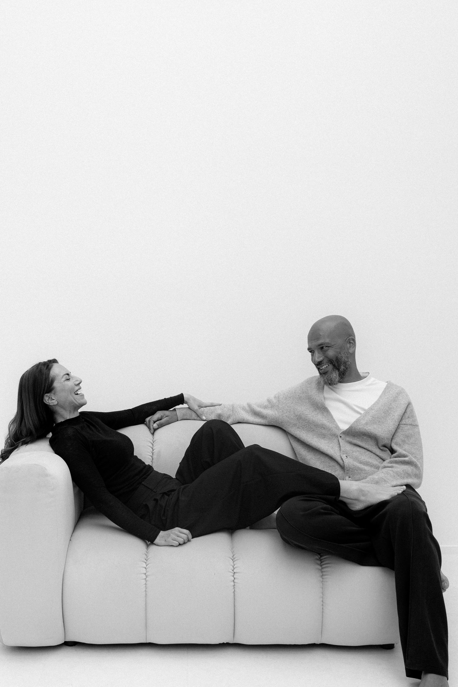 Black and white photo of a smiling couple relaxing together on a white sofa, enjoying a casual conversation.