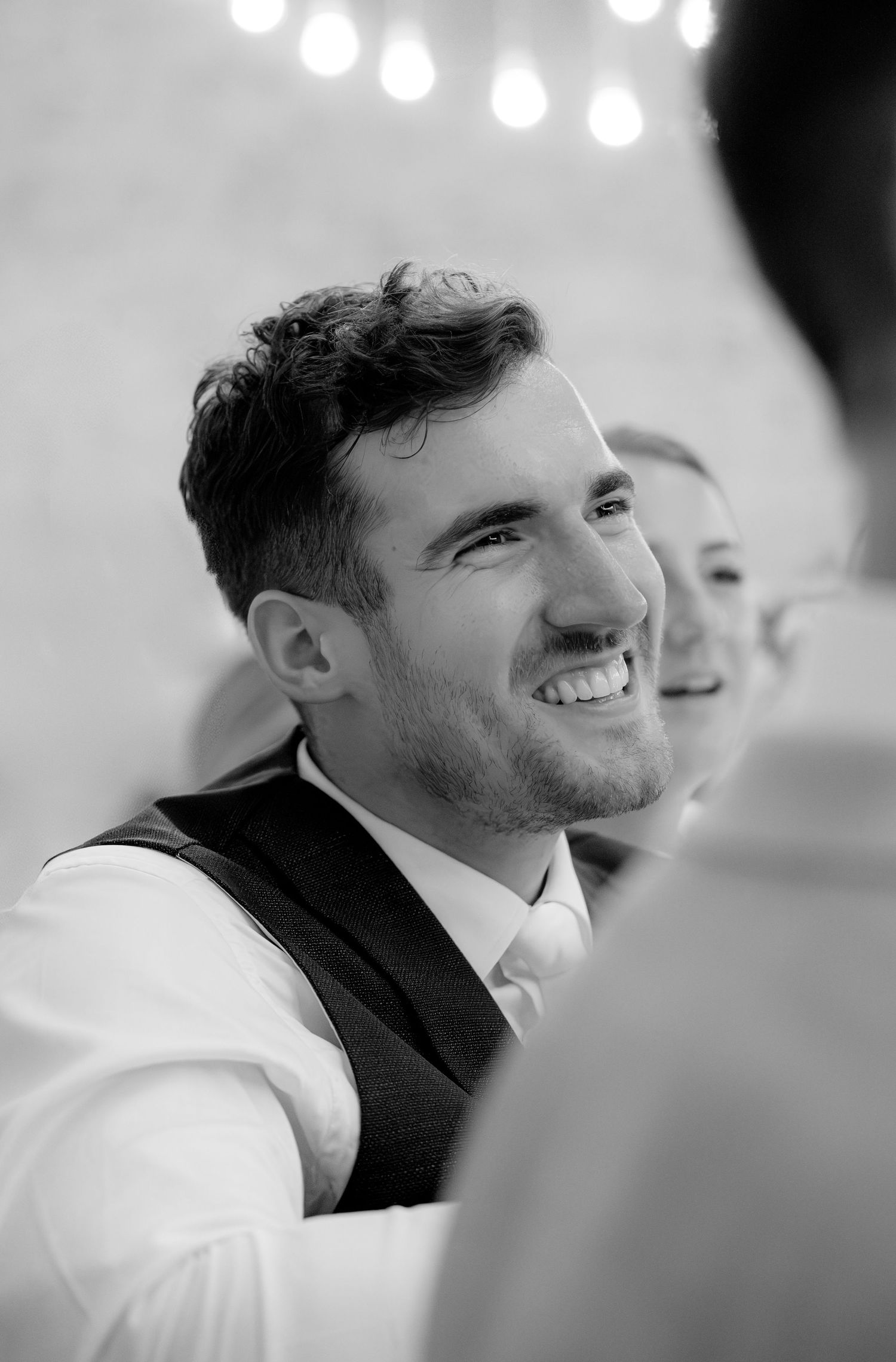 Black and white portrait of smiling guest at formal event with bokeh lights in background.