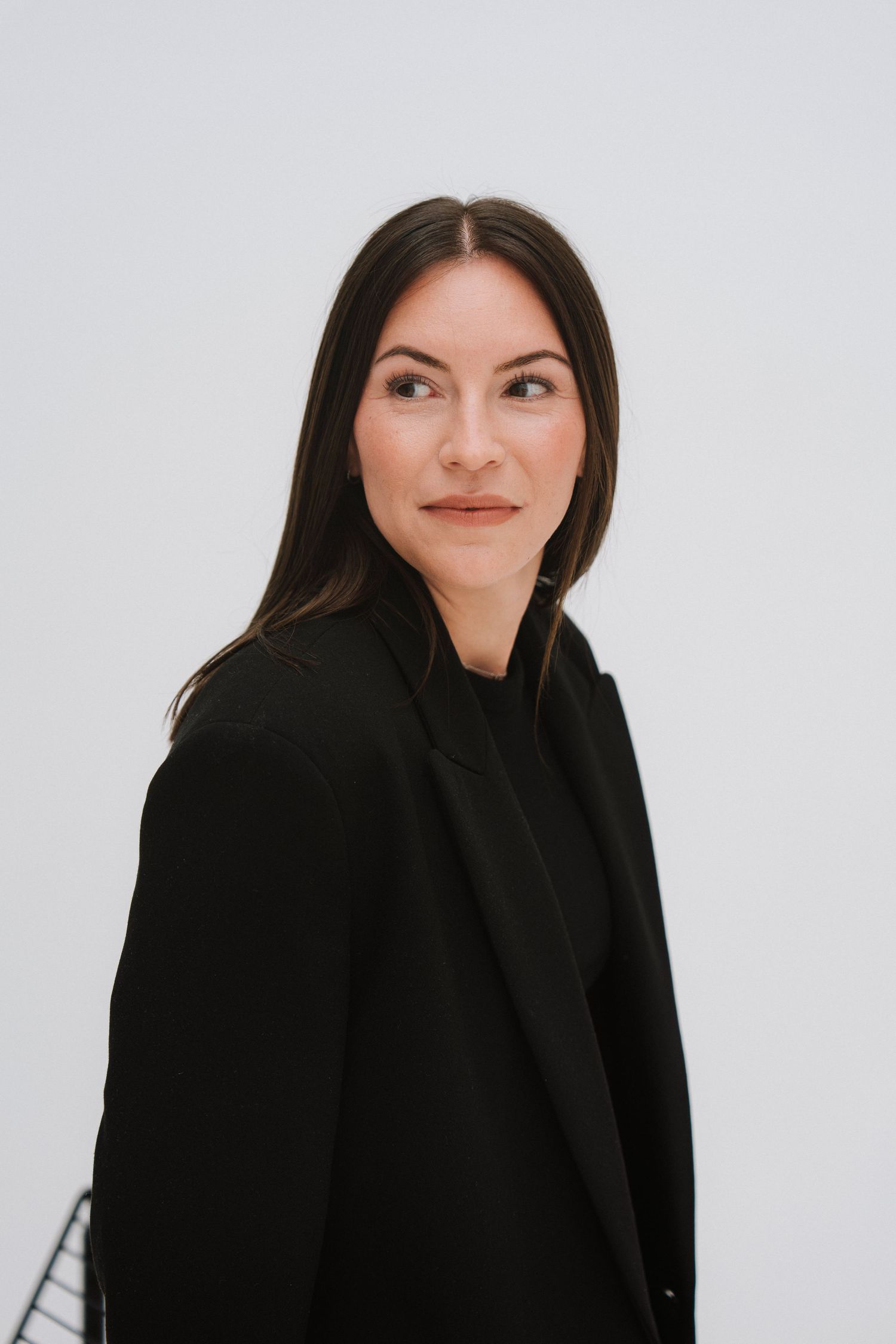 A professional woman with dark hair wearing a black blazer poses confidently against a white background.
