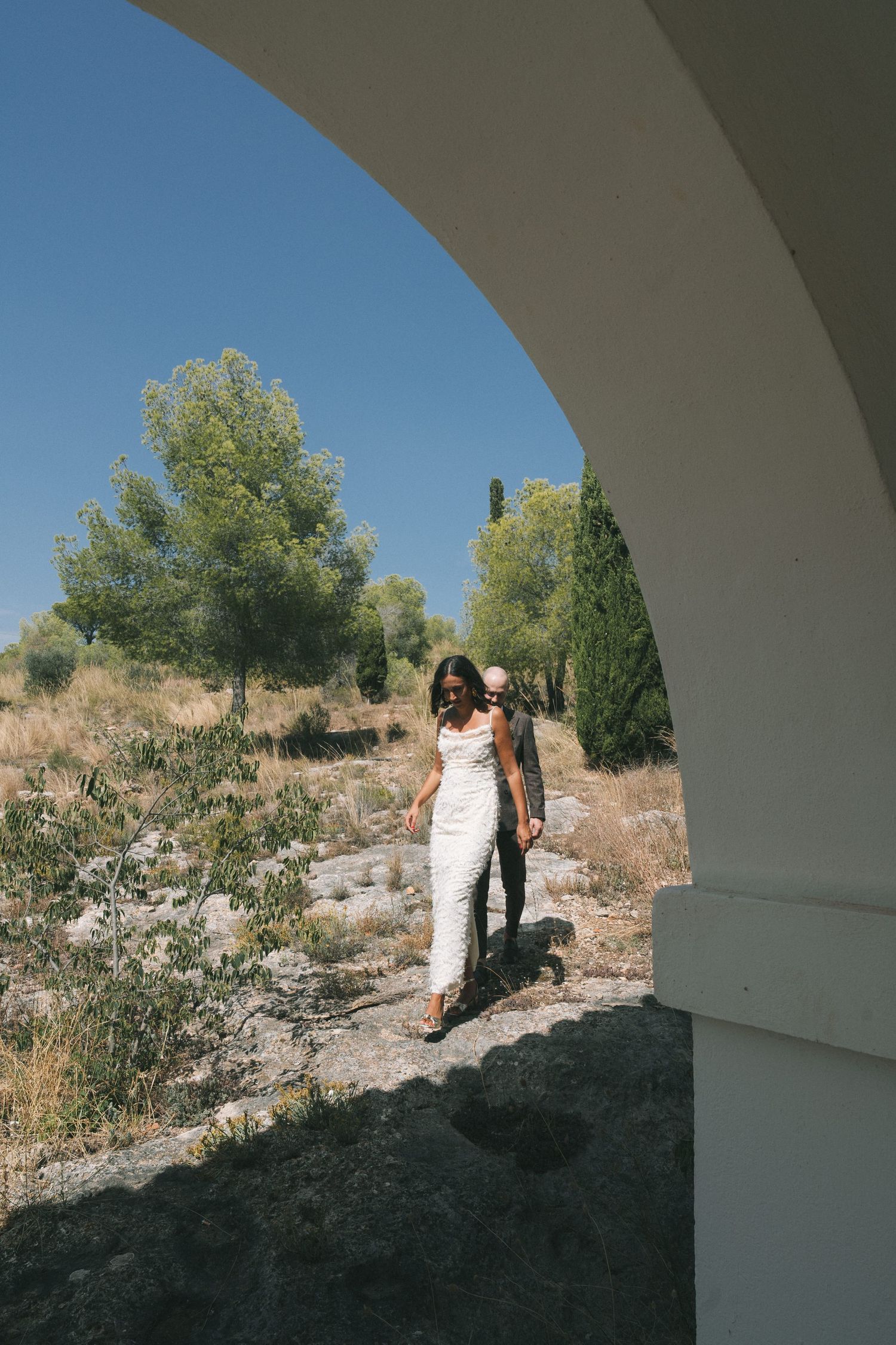 Wedding photography sequence captured under a white archway in a Mediterranean landscape.