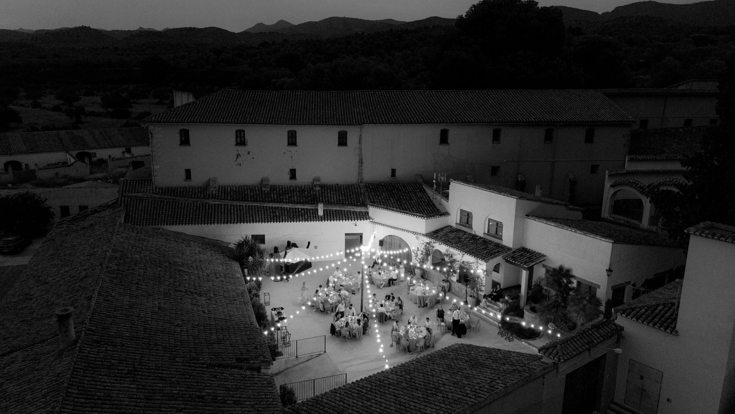 Wide aerial view of an illuminated venue and surrounding landscape at dusk.