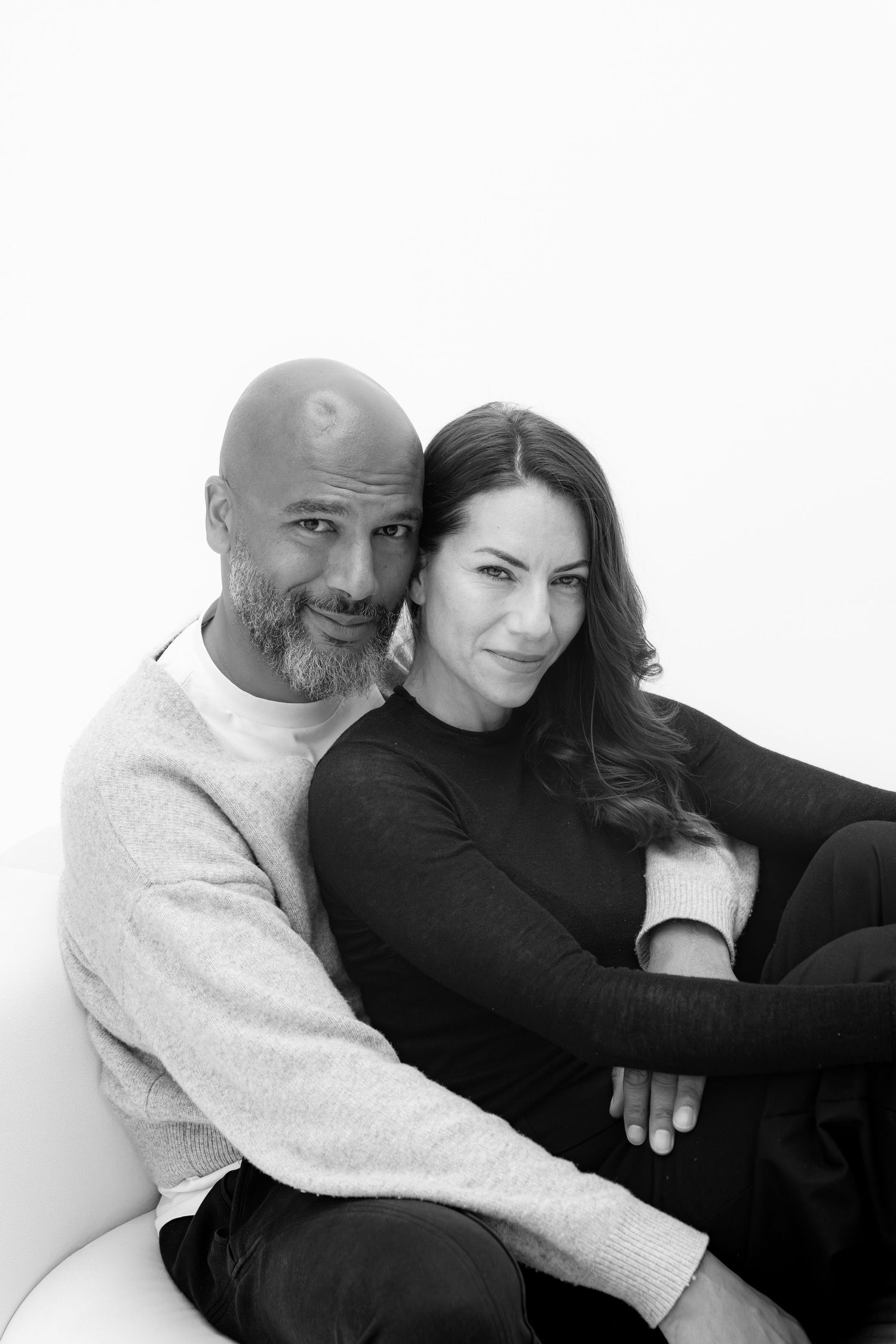 Black and white portrait of a smiling couple sitting together, man with shaved head and beard, woman with long dark hair.