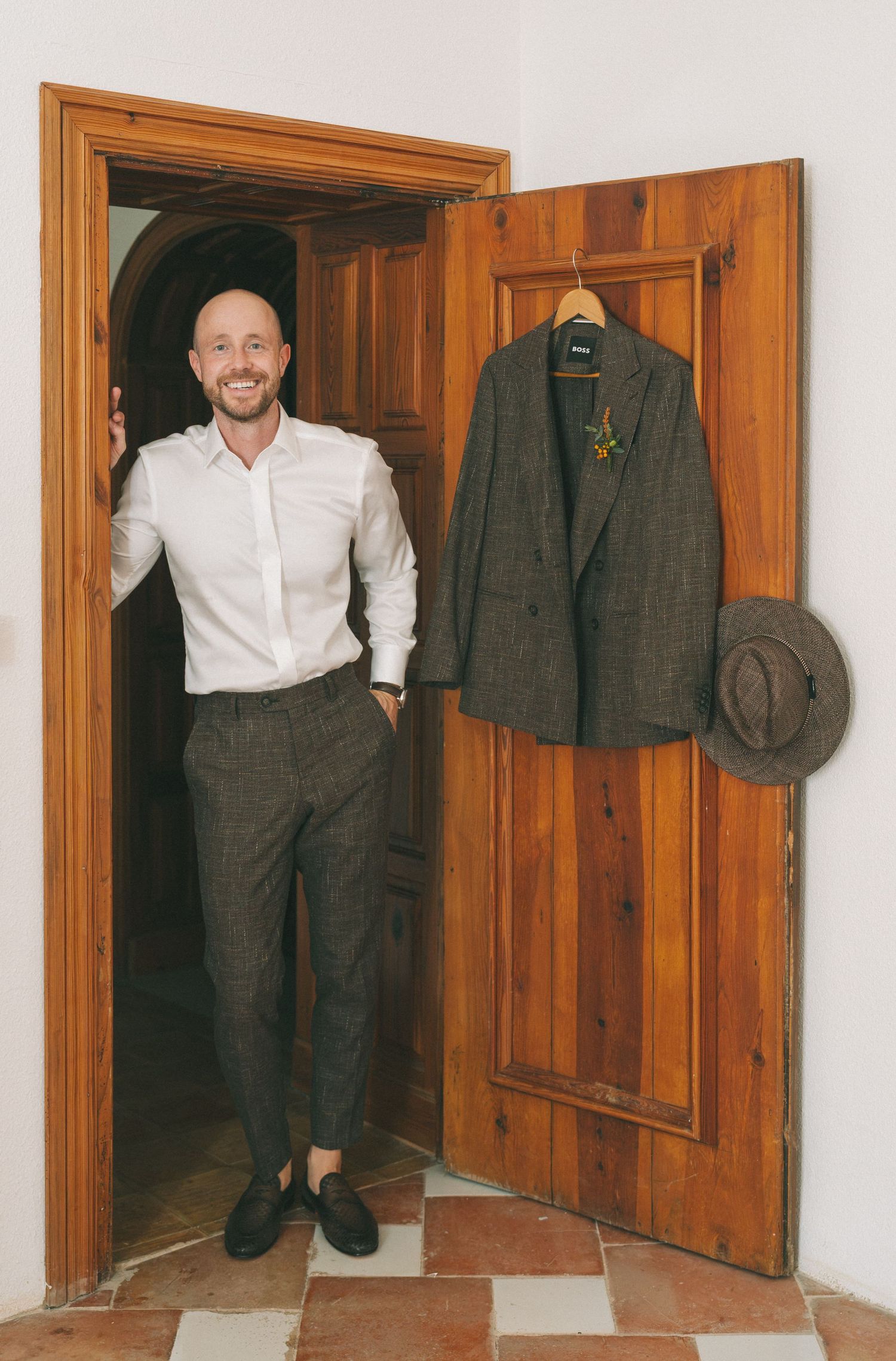 A formal suit jacket hangs on display next to wooden doors in preparation for a wedding.