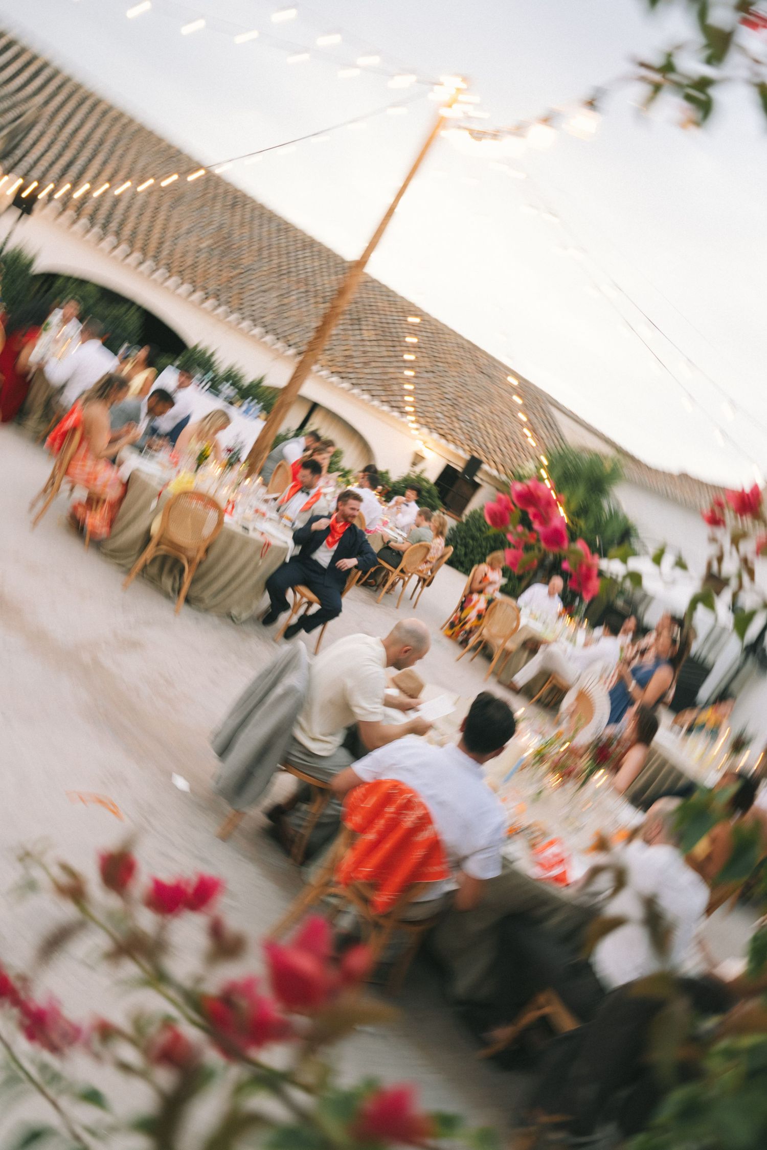 Wedding reception venue with string lights and red flowers in foreground.