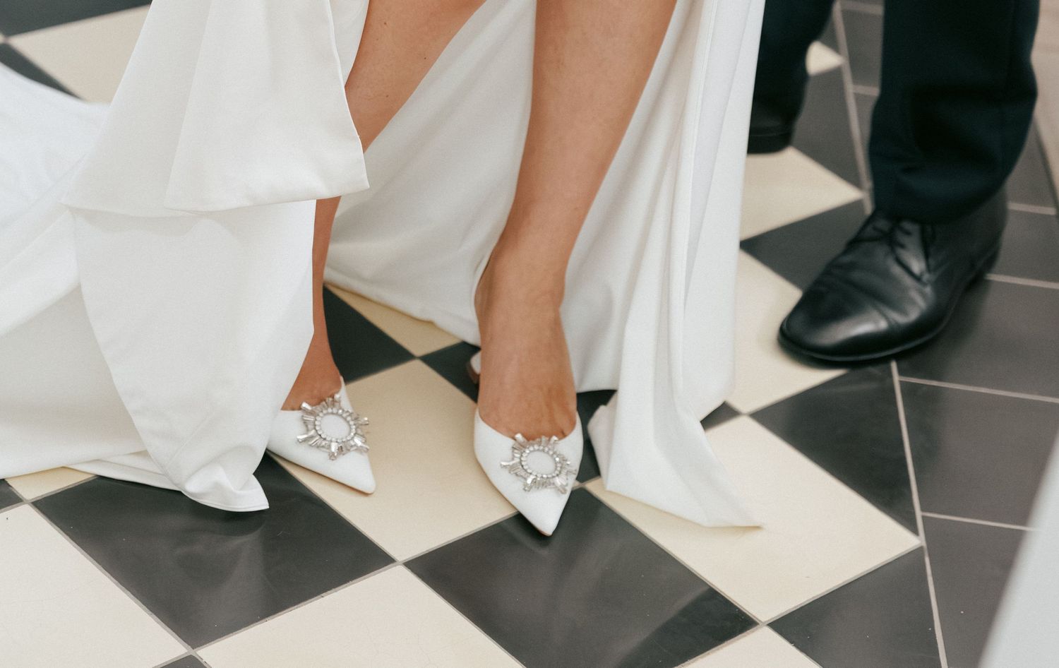 Wedding dress and shoes detail shot on black and white checkered floor.