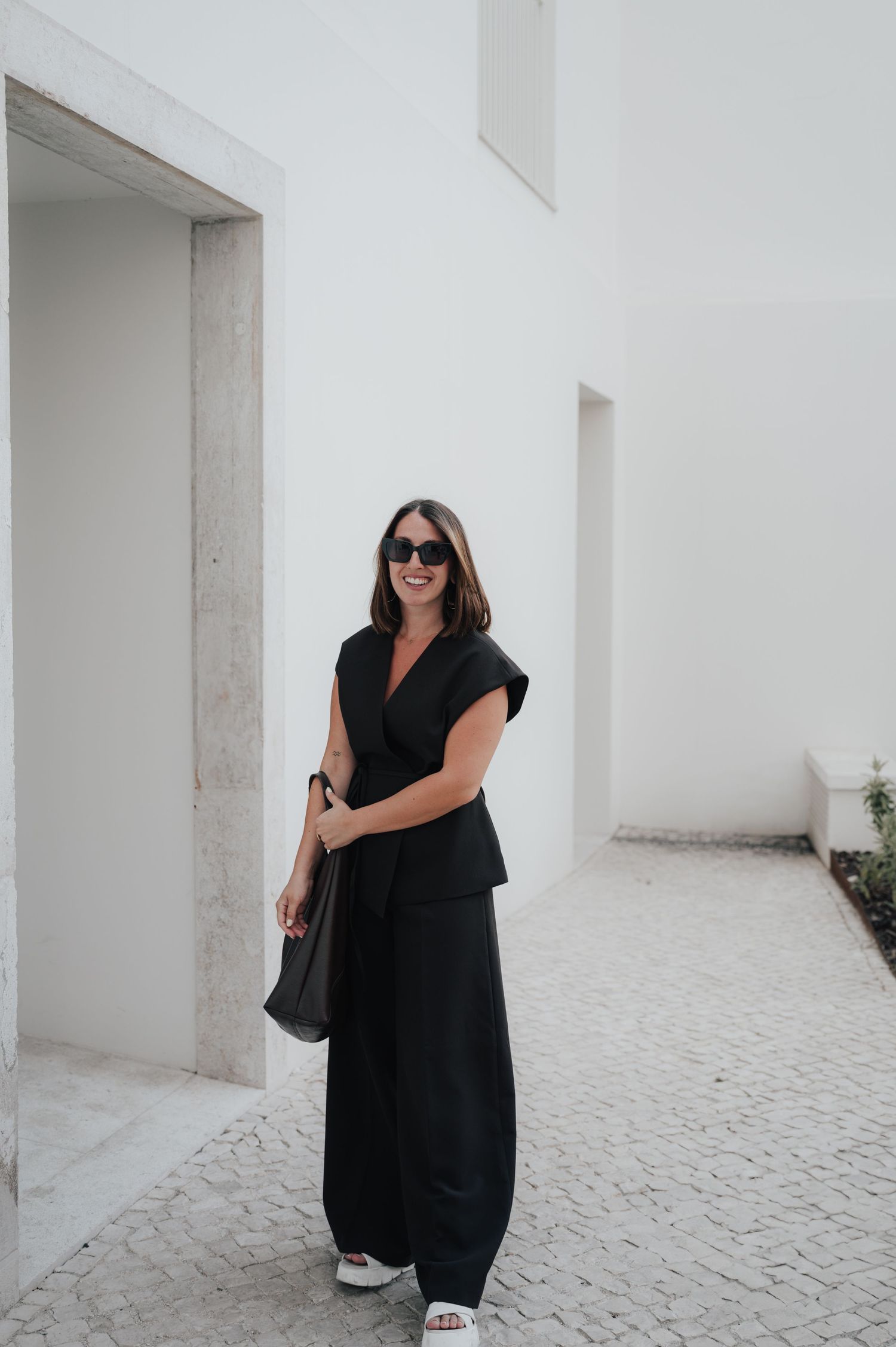 Fashion photoshoot featuring black dress against minimalist white architectural setting.