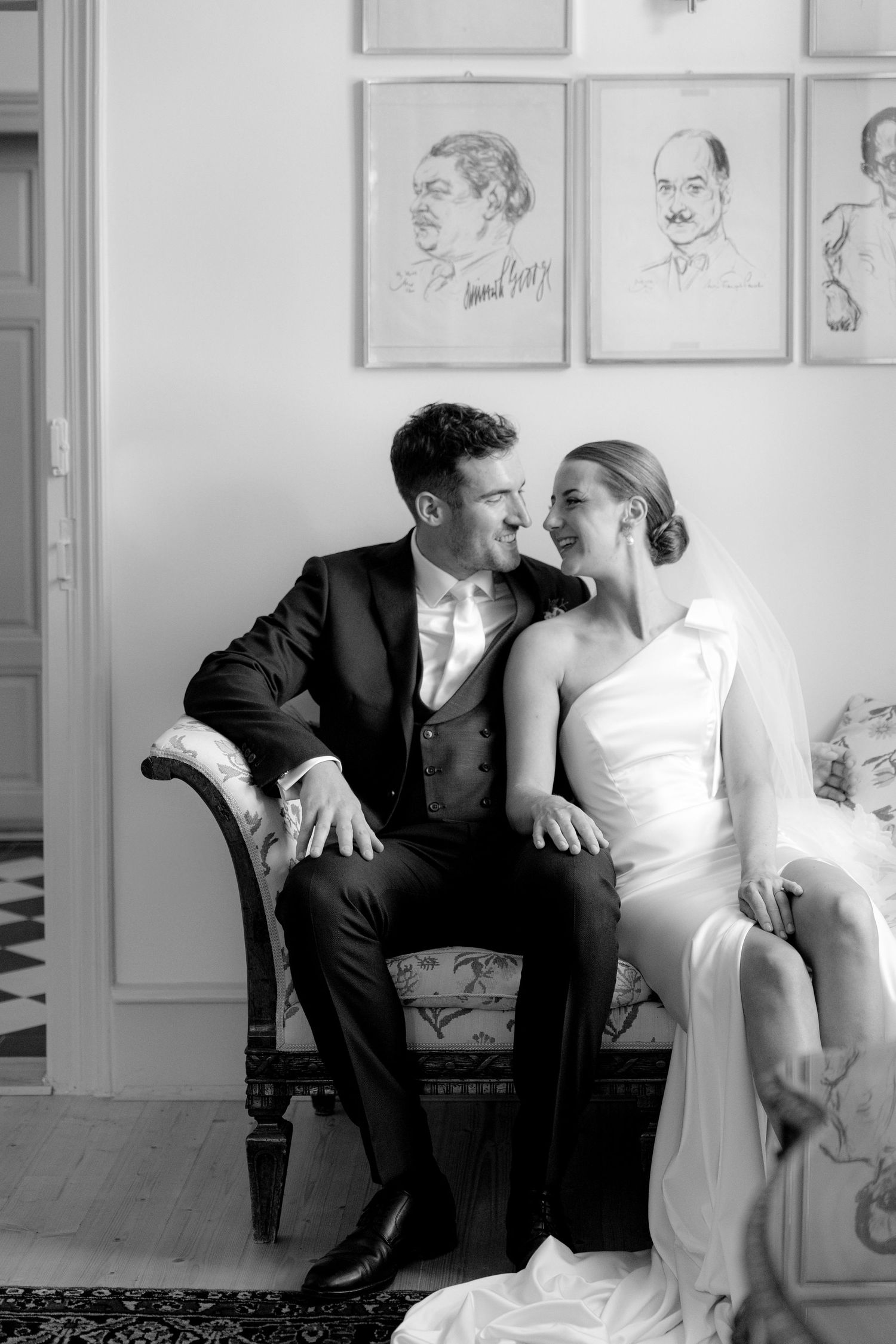 Intimate black and white portrait of a couple seated on an antique sofa.