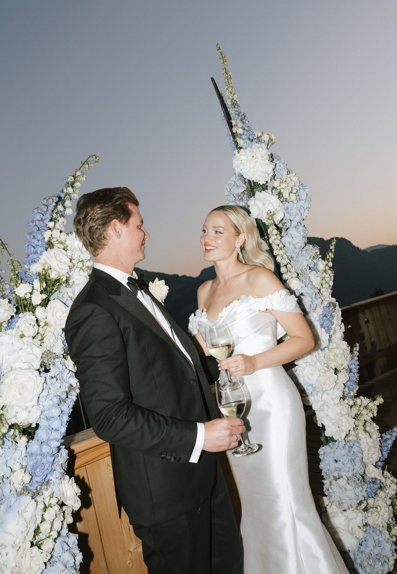 Wedding couple shares an intimate moment under an elegant white floral arch during their ceremony.