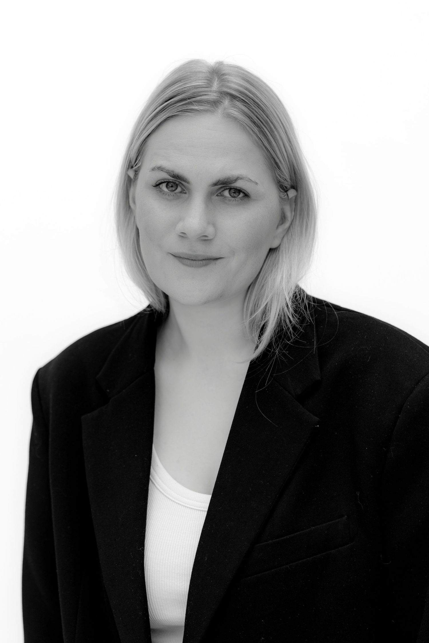Black and white portrait of a blonde woman in an oversized black blazer against a white background.