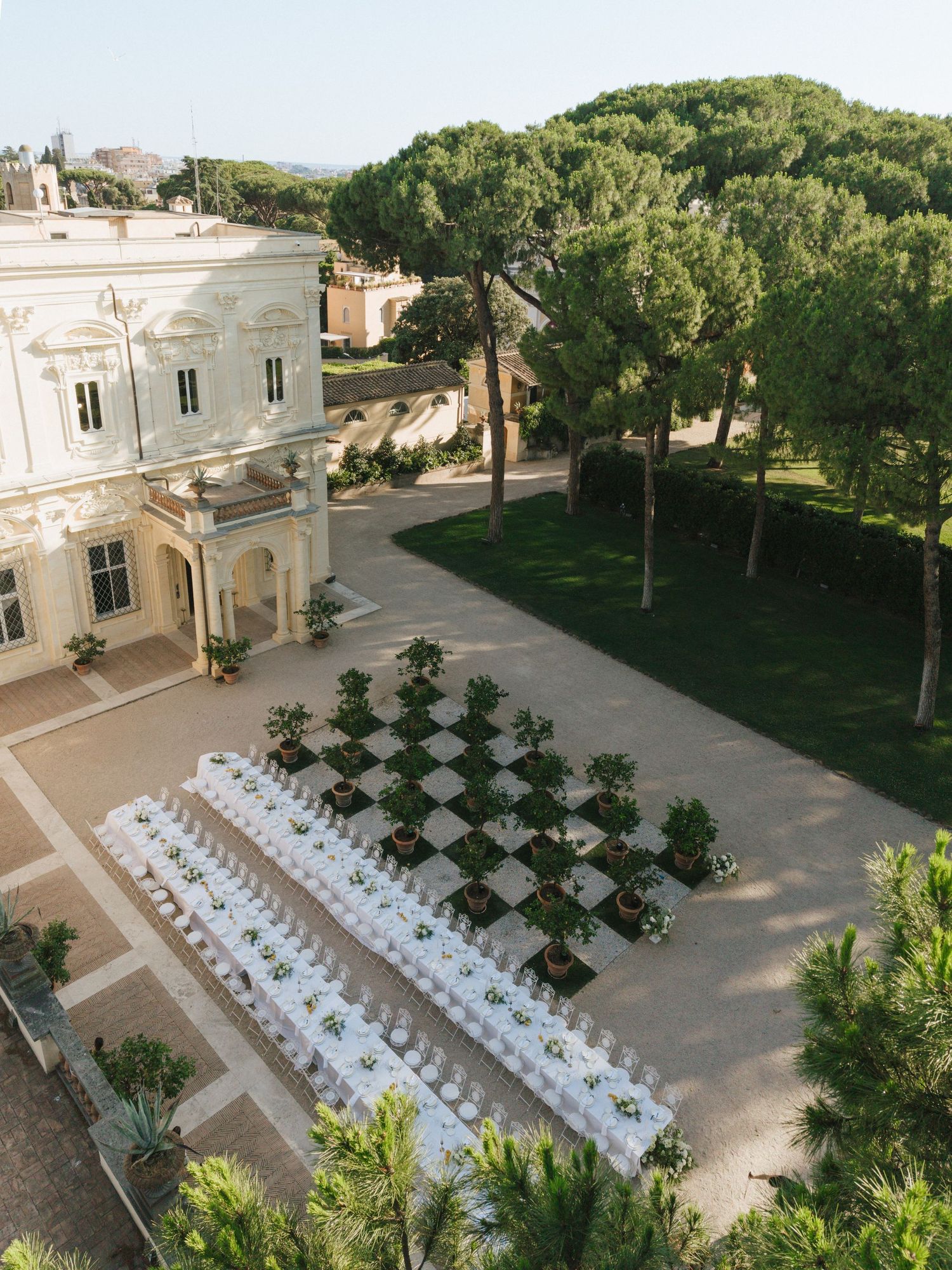 Aerial view of an elegant outdoor wedding reception at a historic Italian villa with long white tables.