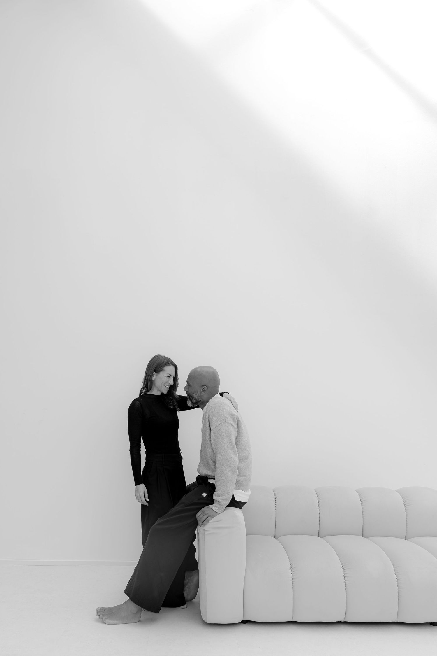 Black and white photo of a couple leaning against a modern white sofa in a minimalist room.
