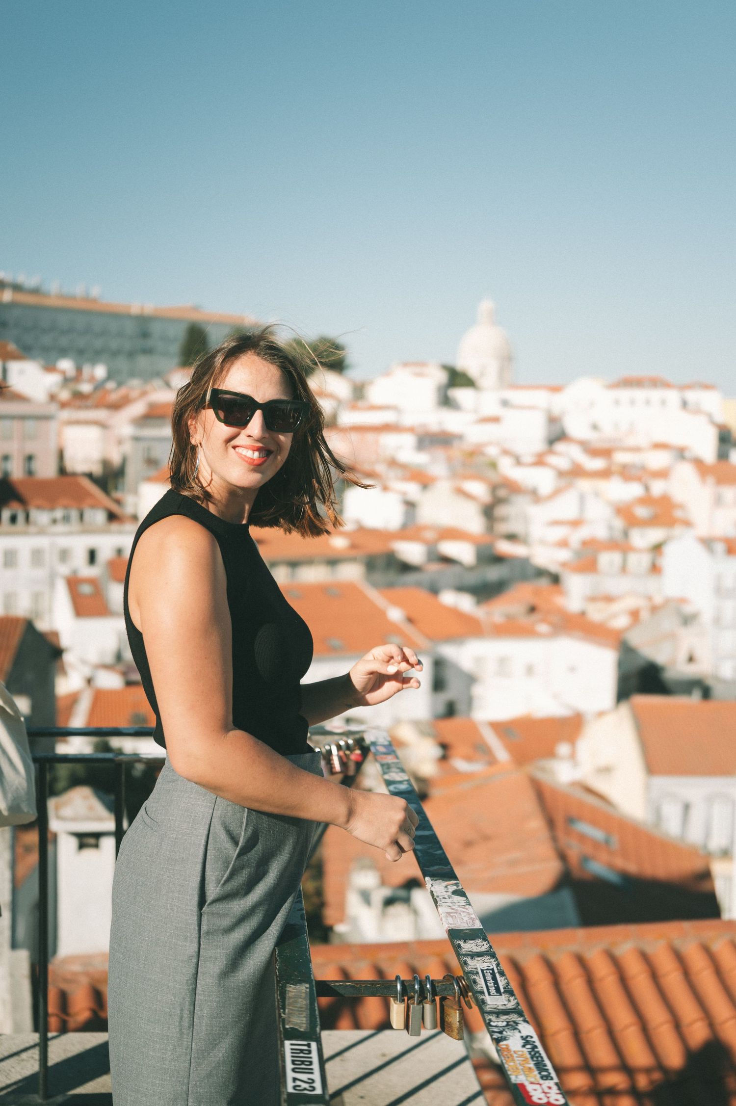 Person enjoying rooftop views of orange-tiled buildings in Lisbon on sunny day.