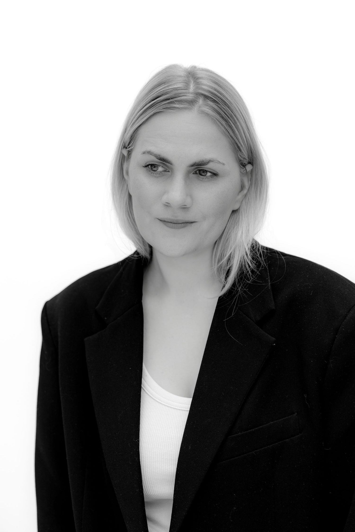 Black and white portrait of a blonde woman in an oversized black blazer and white top against a light background.