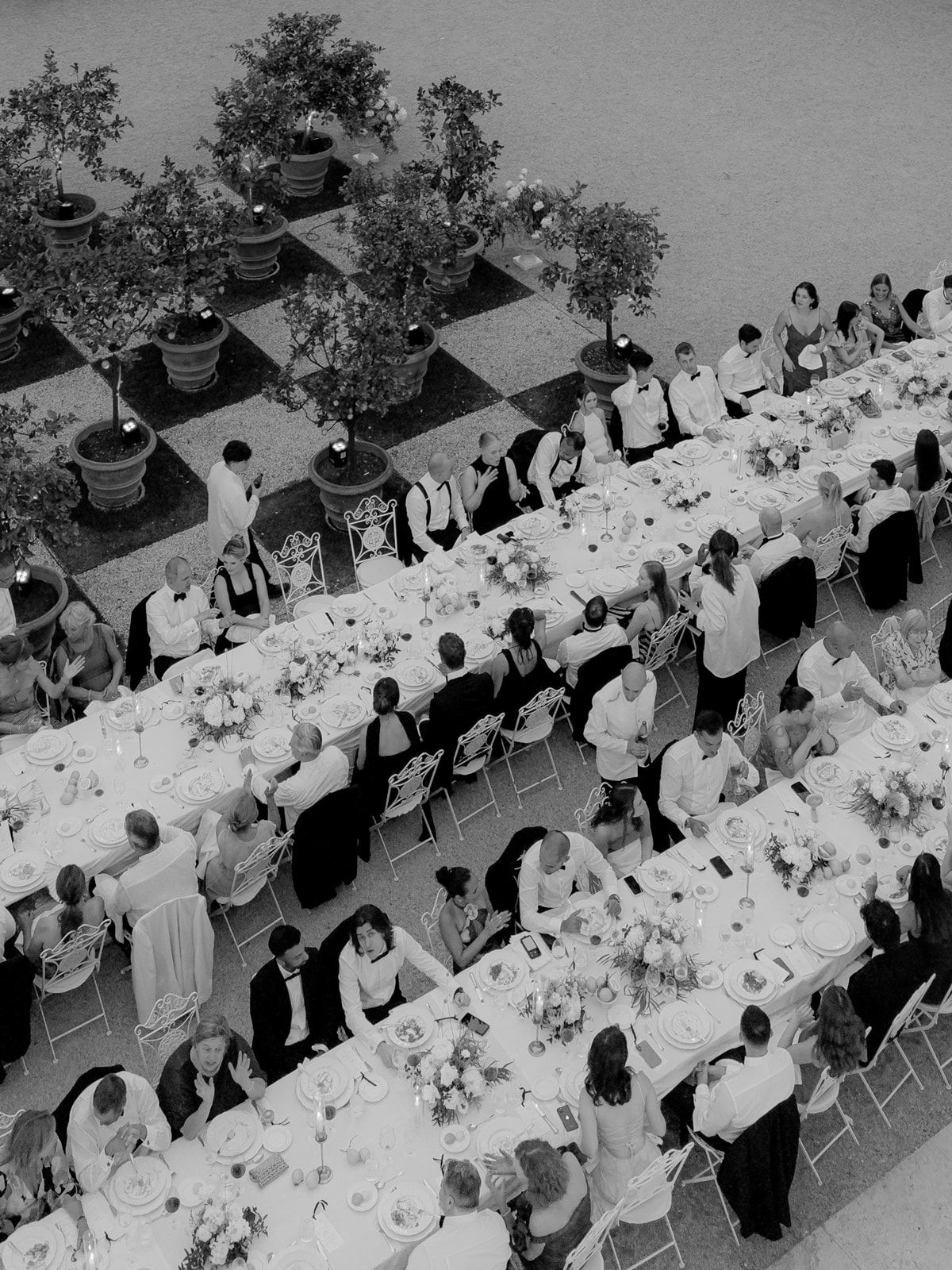 Aerial black and white photo of an elegant outdoor wedding reception with long dining tables and formally dressed guests.