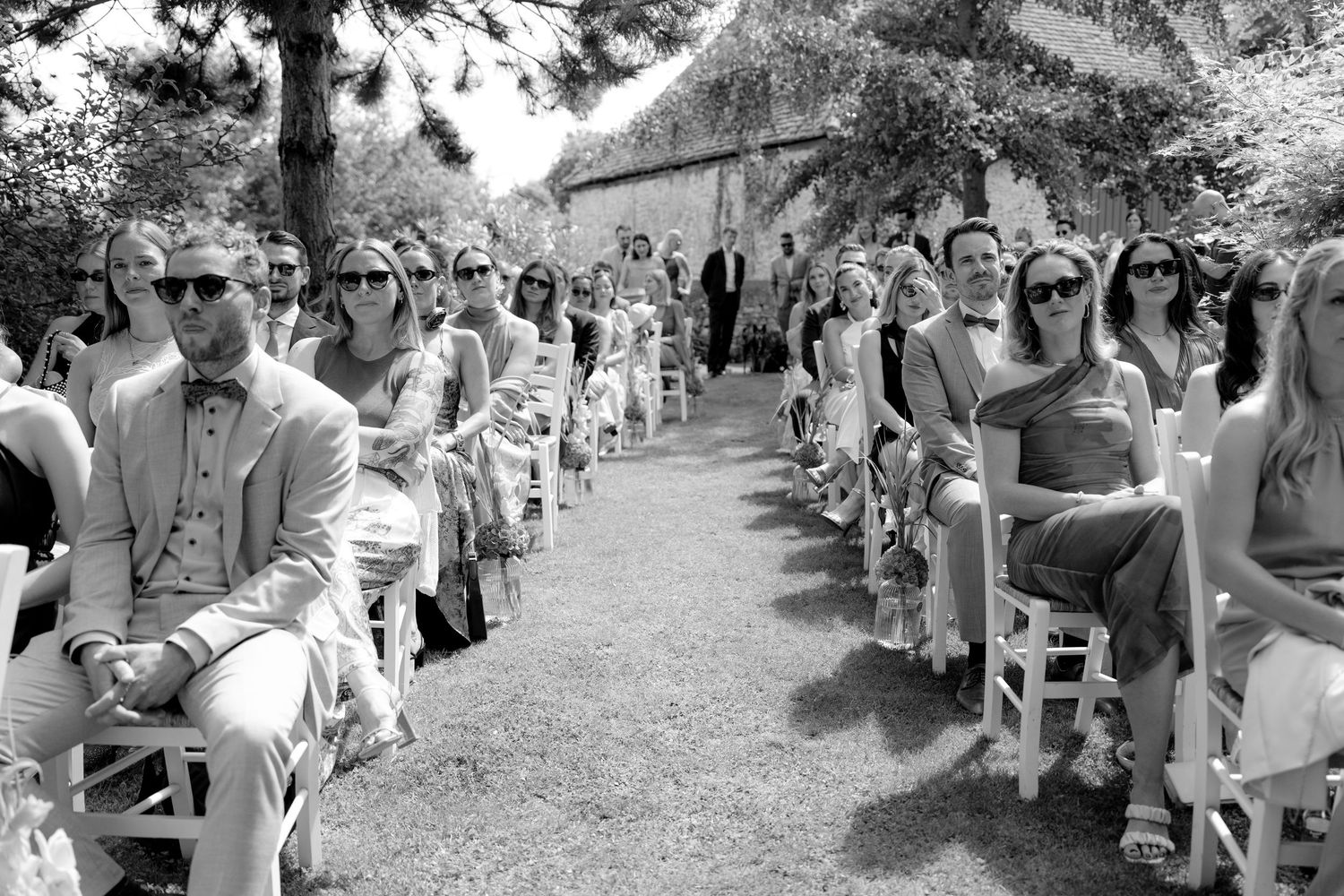 Black and white photo of wedding guests seated outdoors for ceremony.