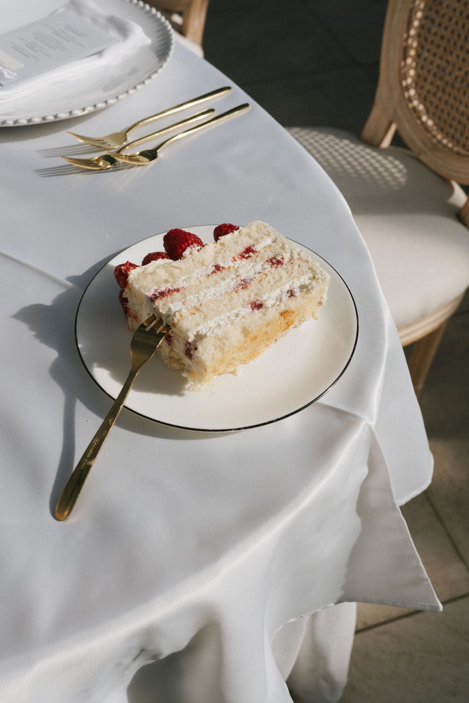 Elegant slice of raspberry cream cake on white plate with gold fork at a wedding reception table.