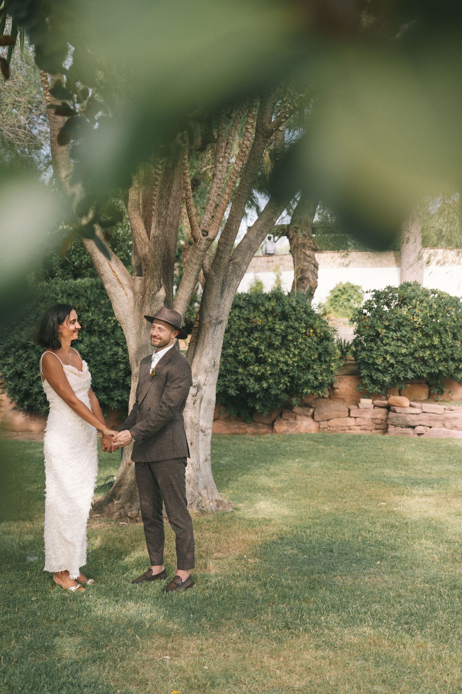 A couple shares a moment together under trees in a garden setting.