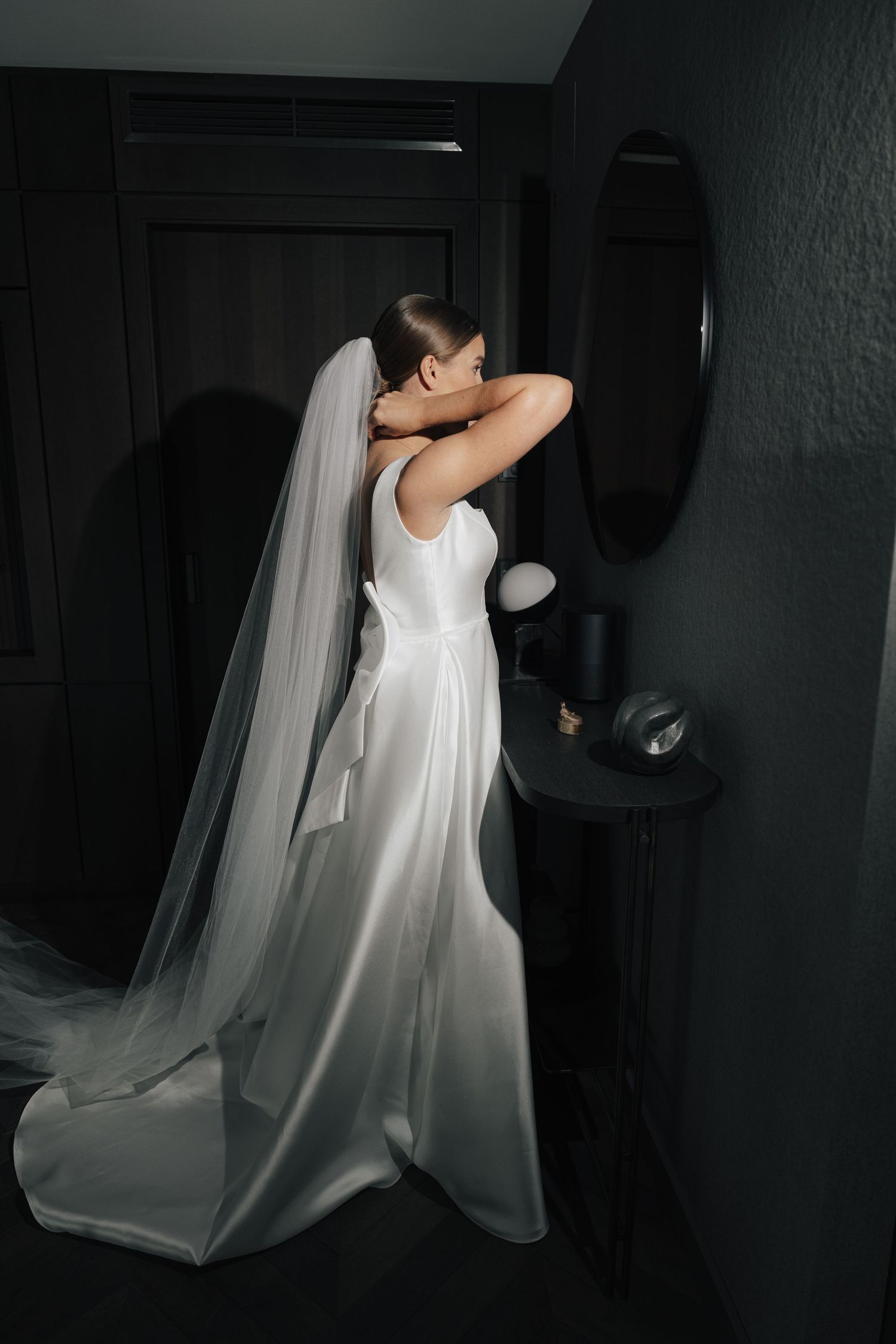 White wedding dress with flowing veil captured in dramatic dark lighting.