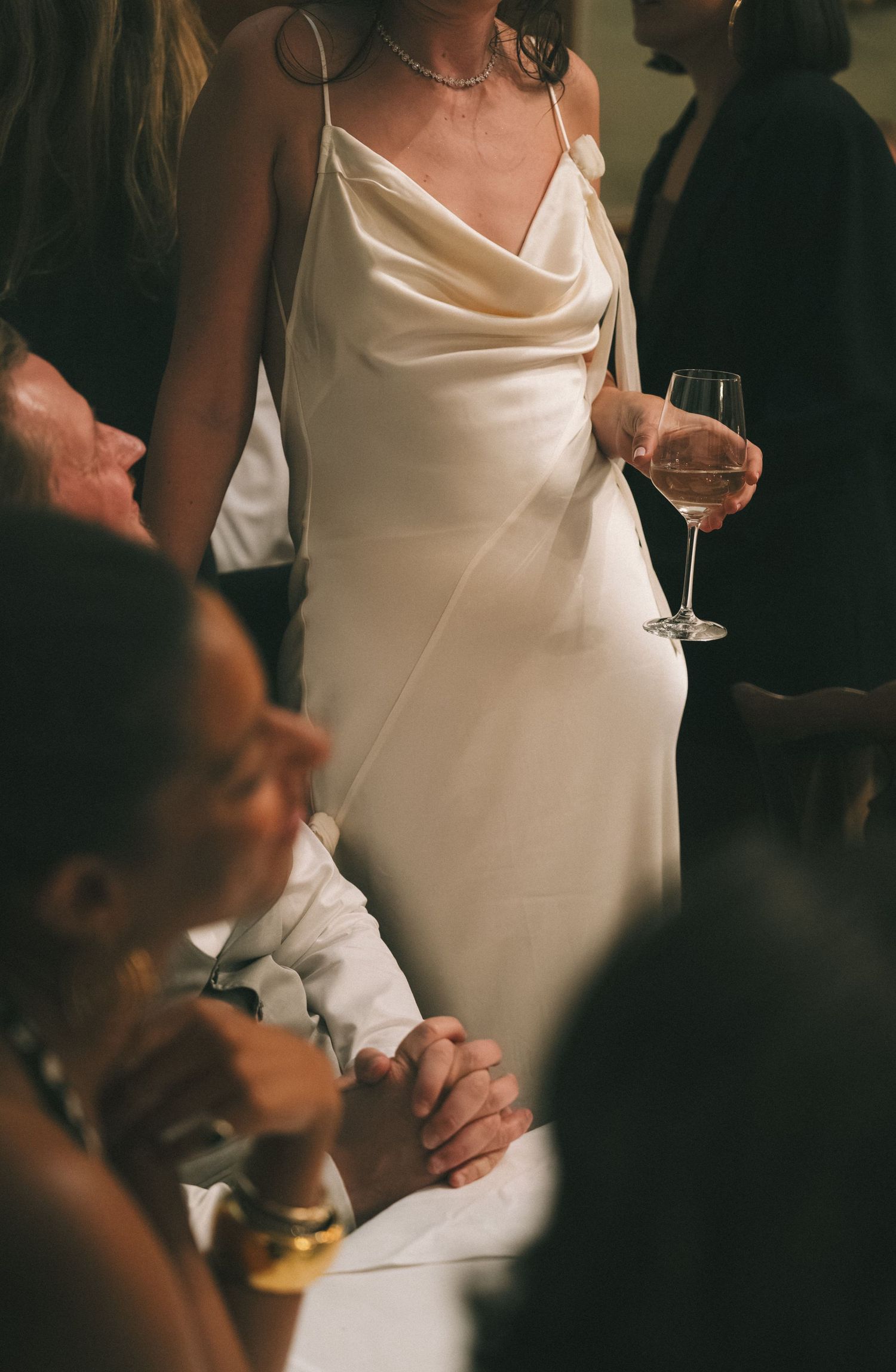 Bride in elegant white satin slip dress holding a glass of rosé wine at a wedding reception.