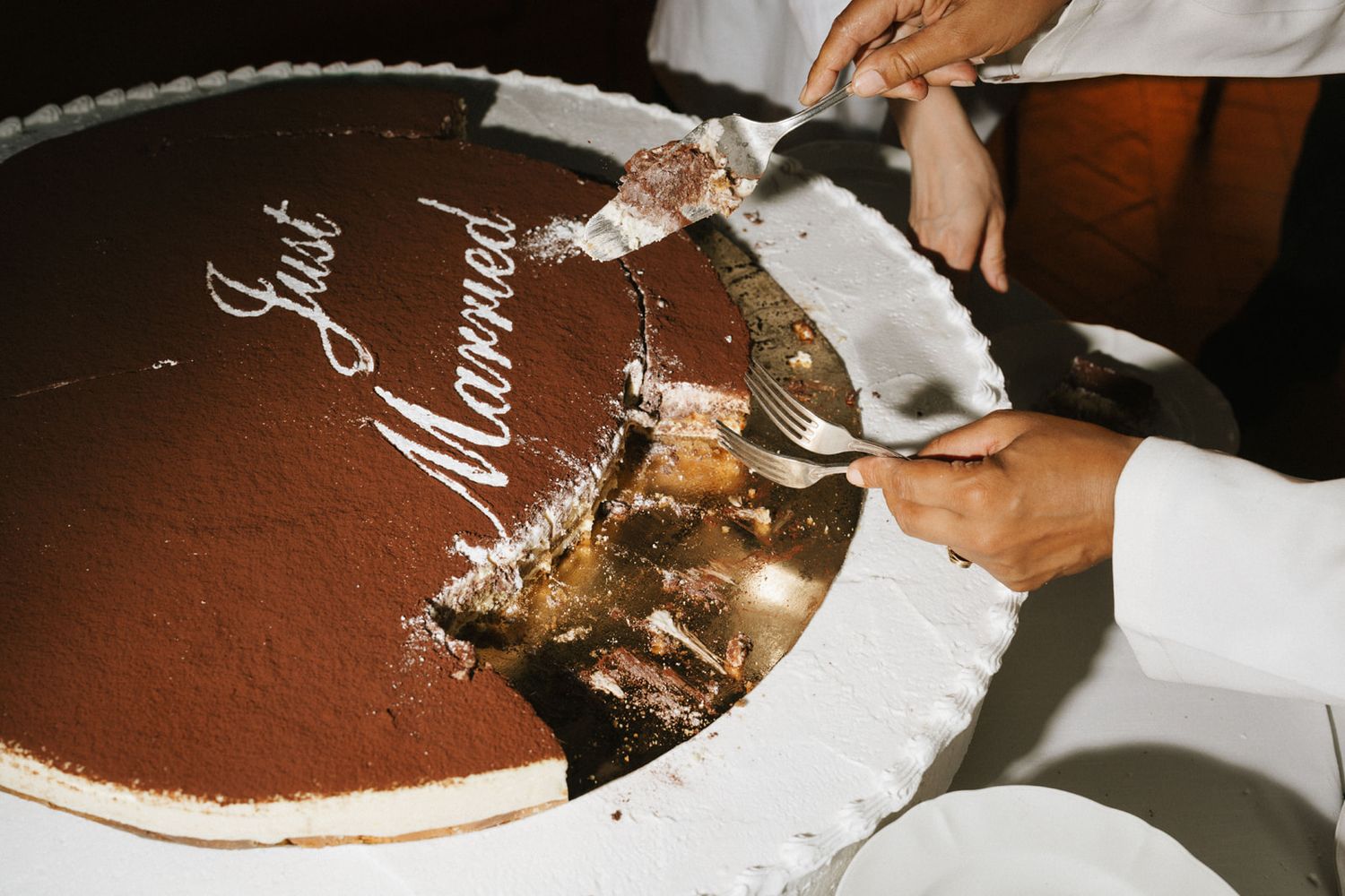 Couple cutting a large chocolate tiramisu wedding cake decorated with Just Married text at their reception.