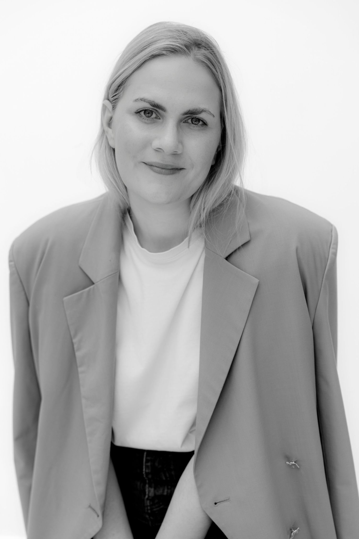 Black and white portrait of a blonde woman in an oversized blazer and white t-shirt posing confidently.