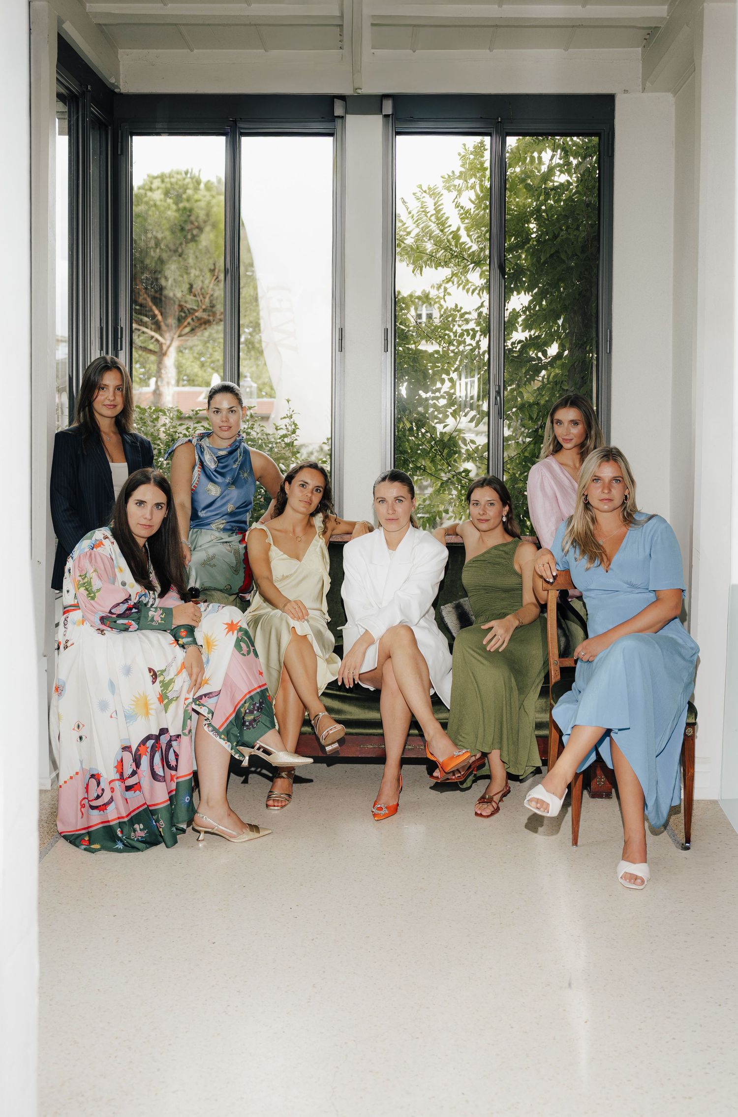 Group relaxing on a white porch wearing colorful floral and pastel dresses.