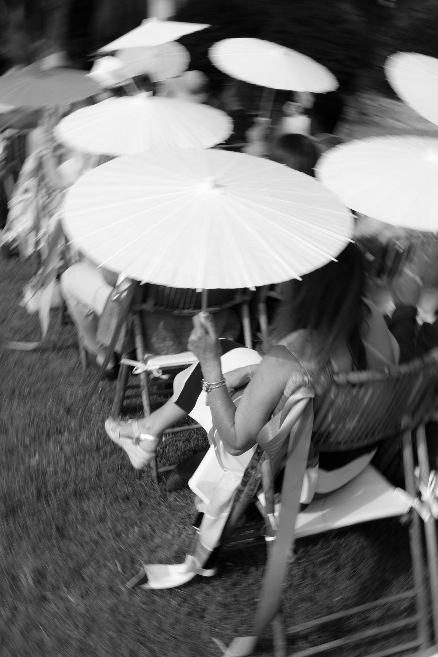 Motion-blurred black and white image of guests with white parasols.