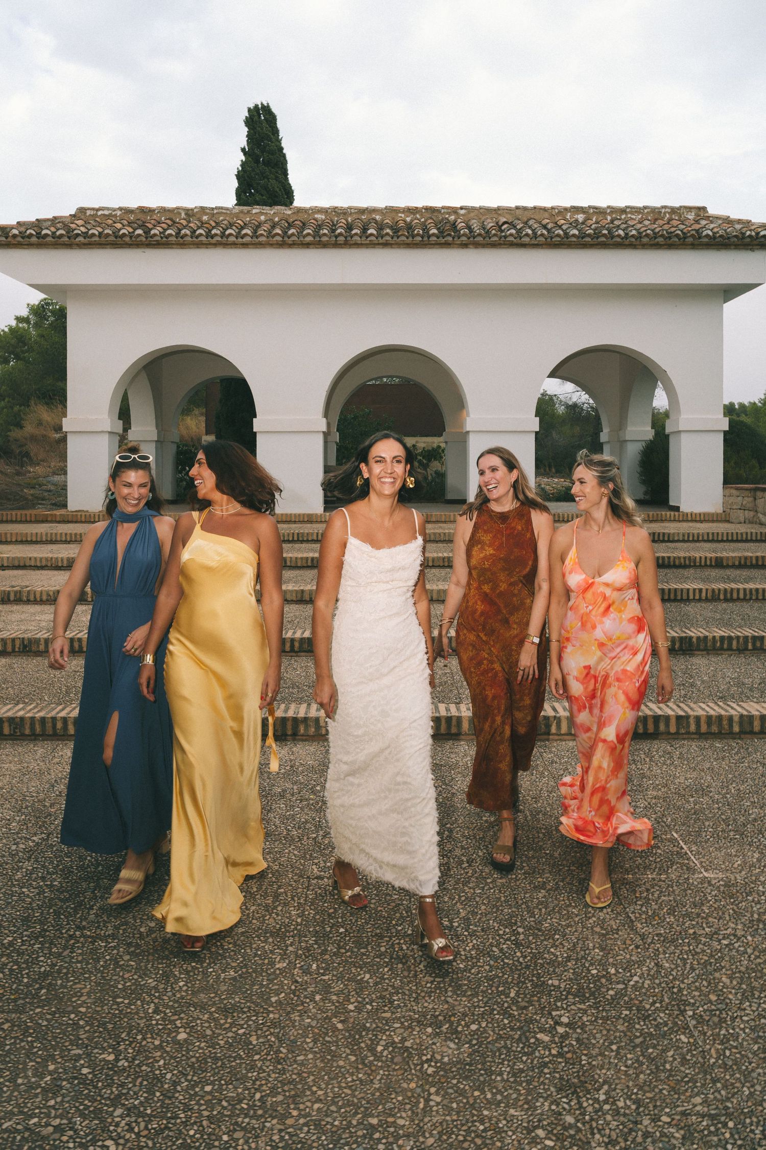 Group walking along a Spanish colonial building wearing colorful summer dresses.