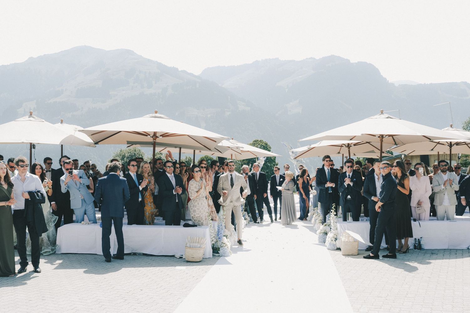 Panoramic view of a mountain wedding reception with white umbrellas and gathered guests.