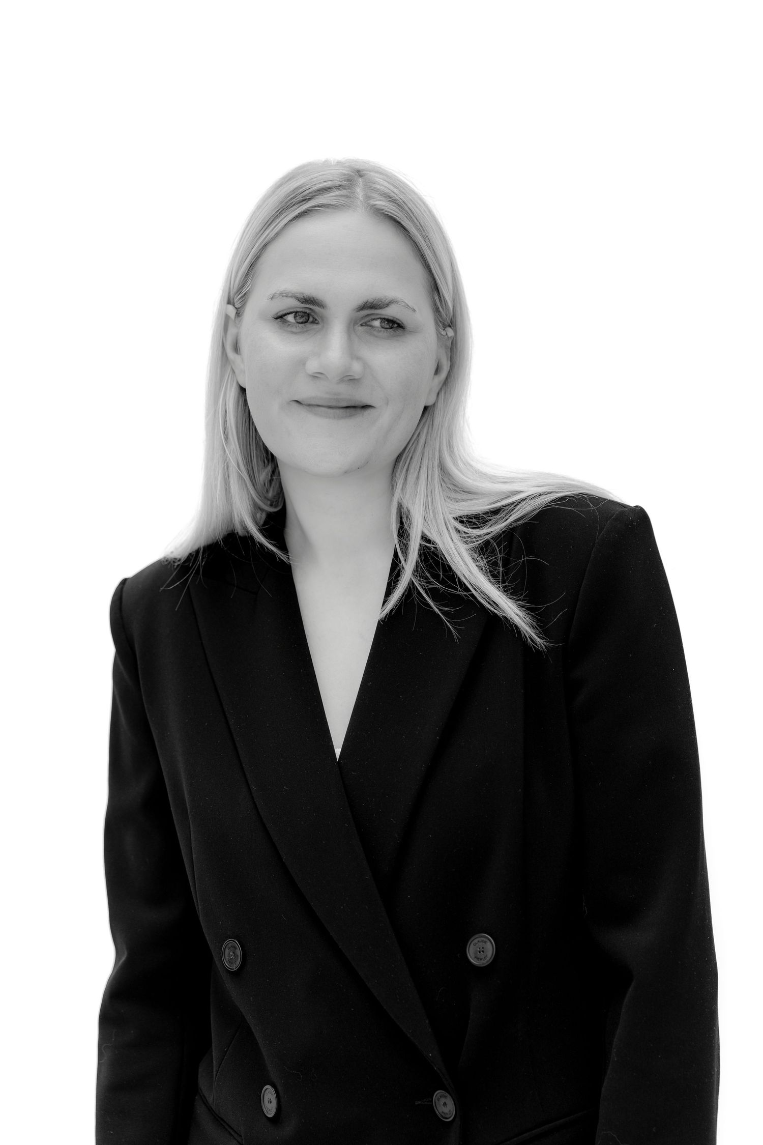 Black and white portrait of a blonde woman in a dark blazer smiling confidently against a white background.