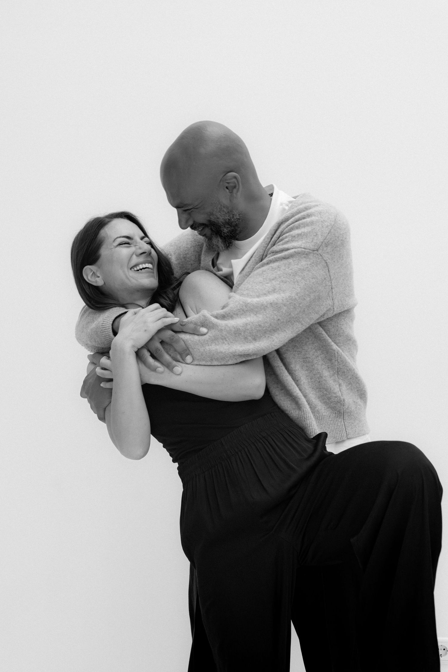 Black and white photo of a laughing couple embracing warmly against a white background.