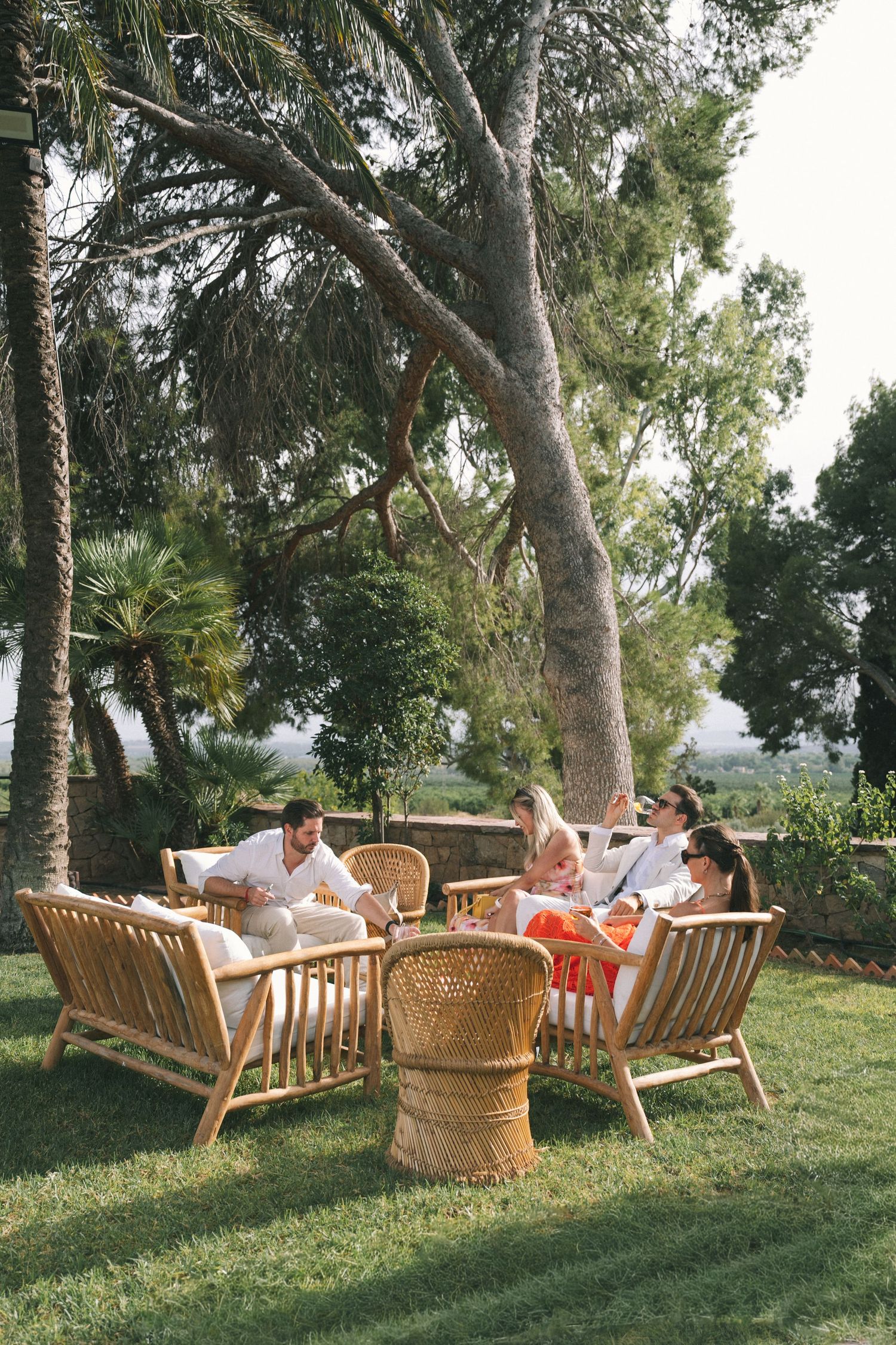 Guests relaxing in rattan furniture under palm trees at outdoor garden party.