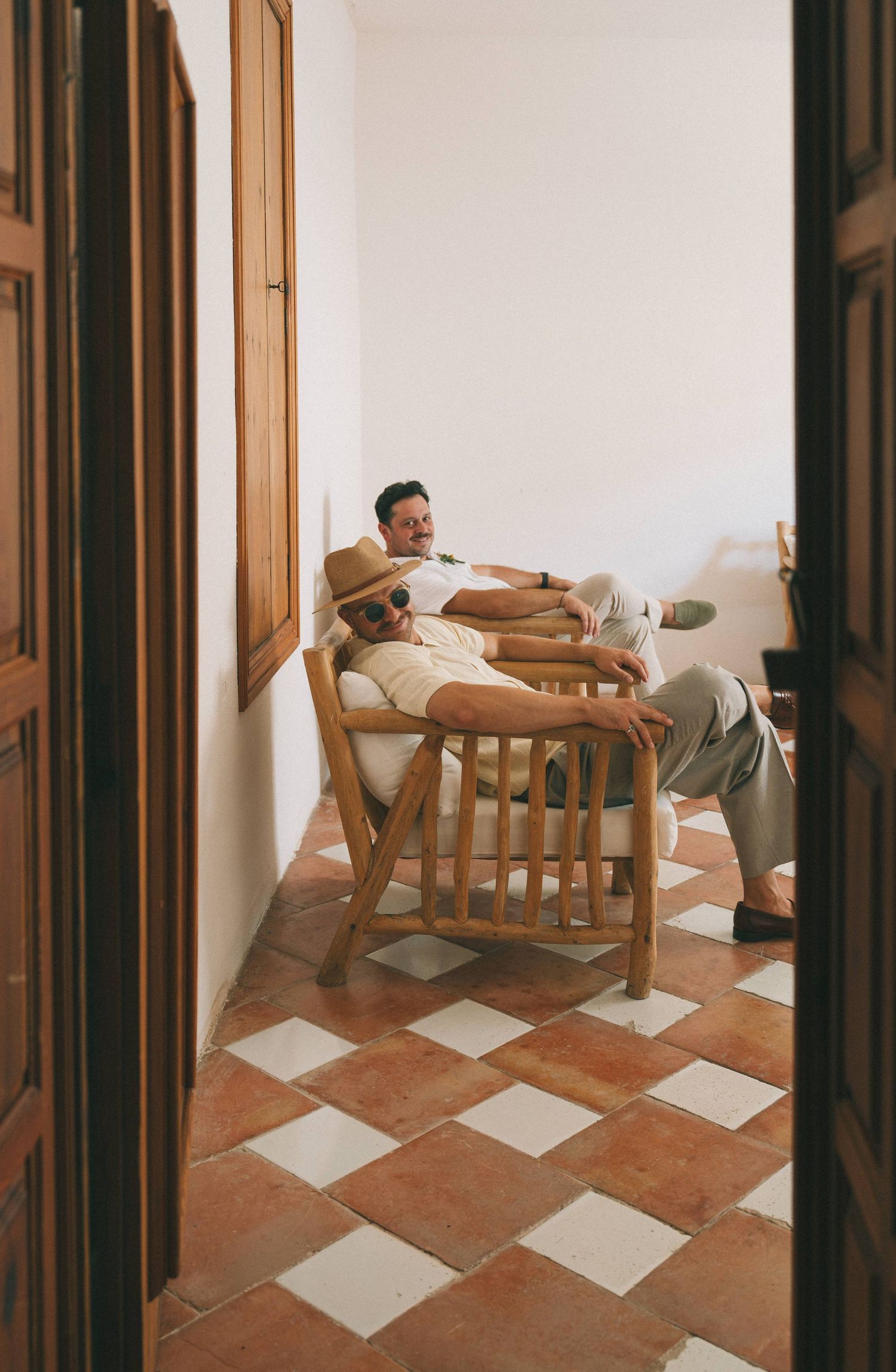 People relaxing in wooden chairs on a tiled floor during a wedding event.