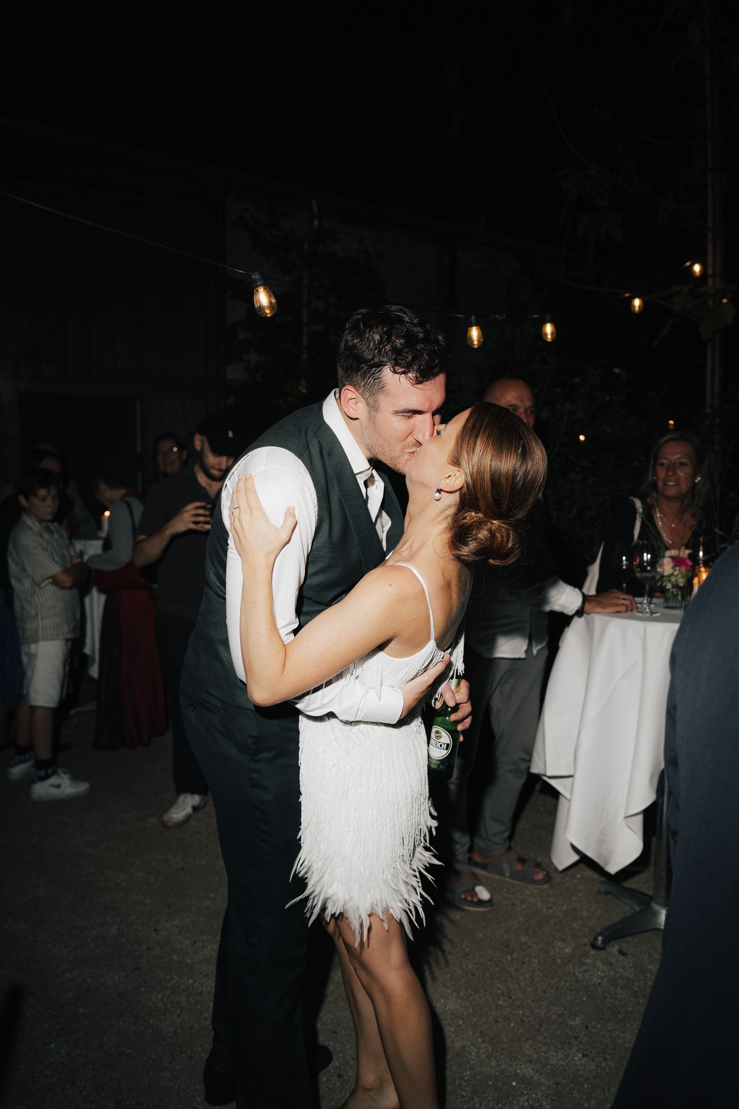 Couple dancing at night event with string lights visible in background.