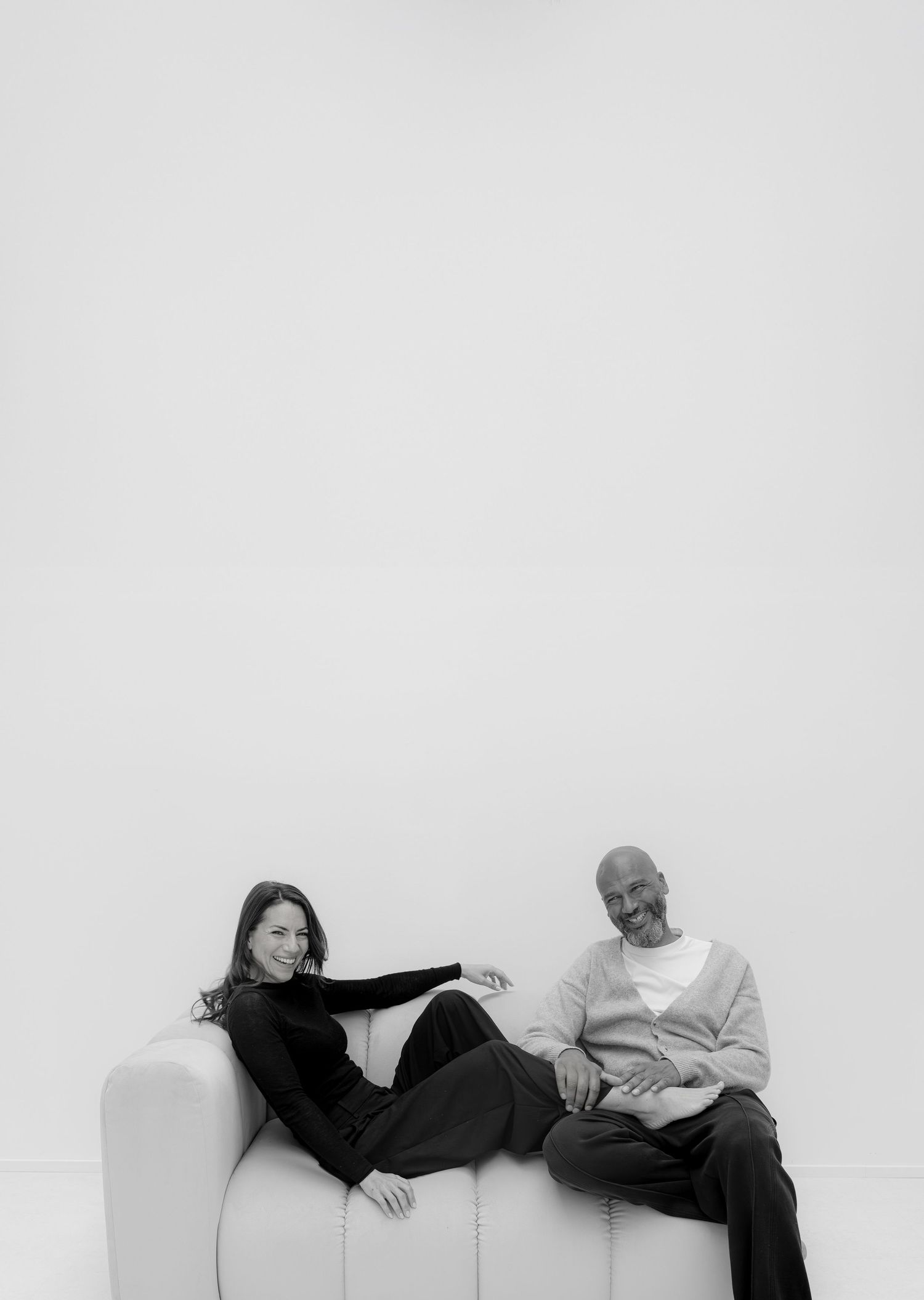 Black and white photo of a man and woman relaxing together on a white sofa, smiling at the camera.